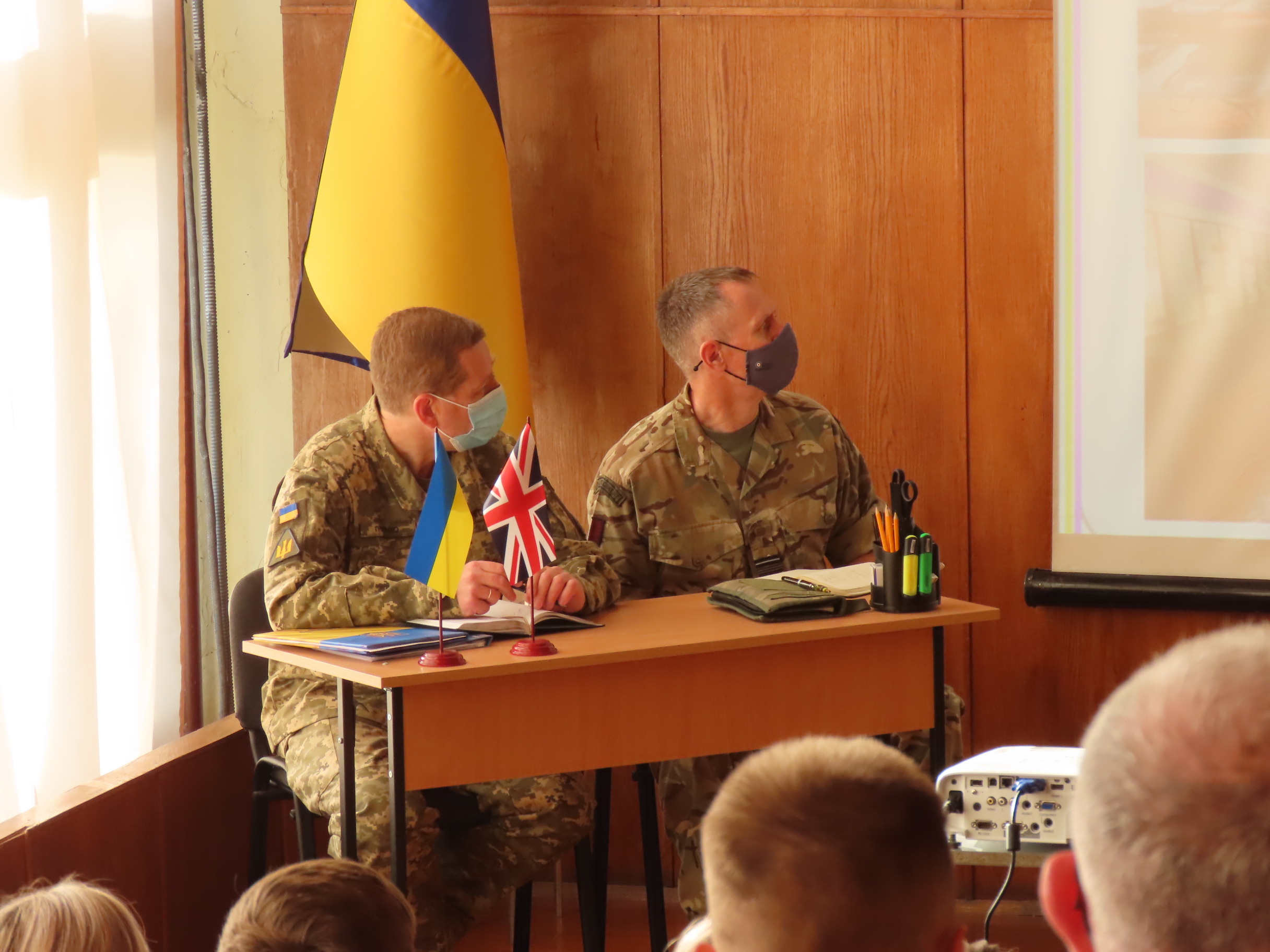 Personnel sit at desk with Ukrainian flag.