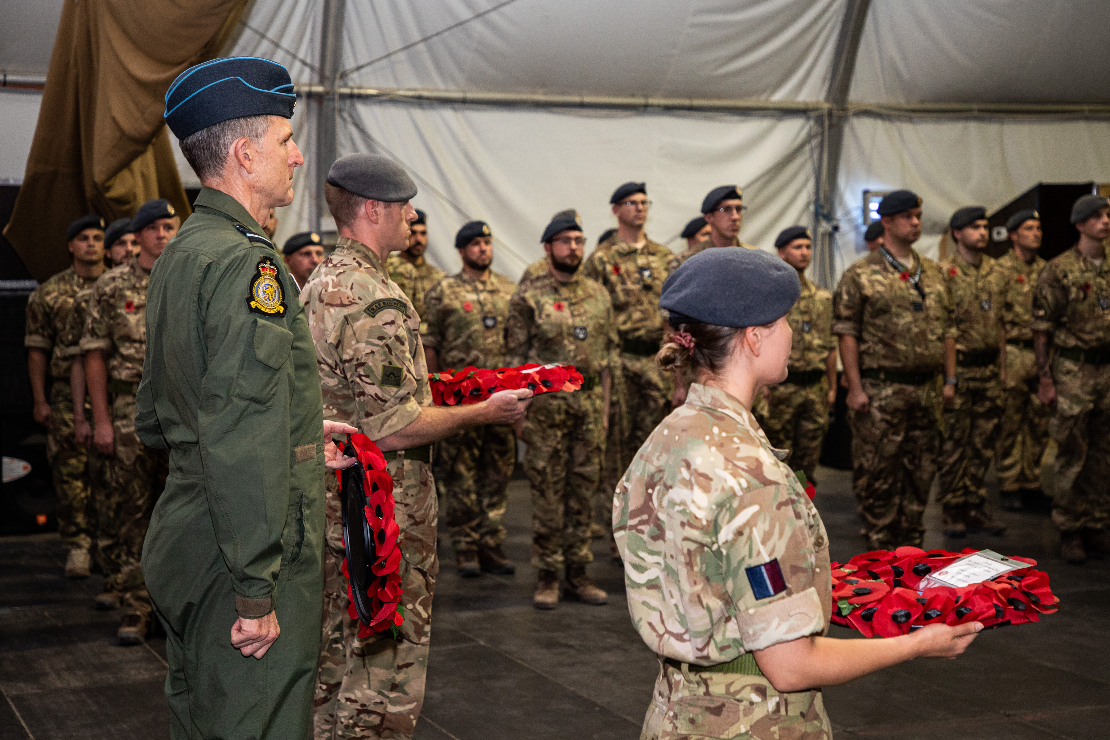 Personnel stand inside tent with three holding poppy wreaths.