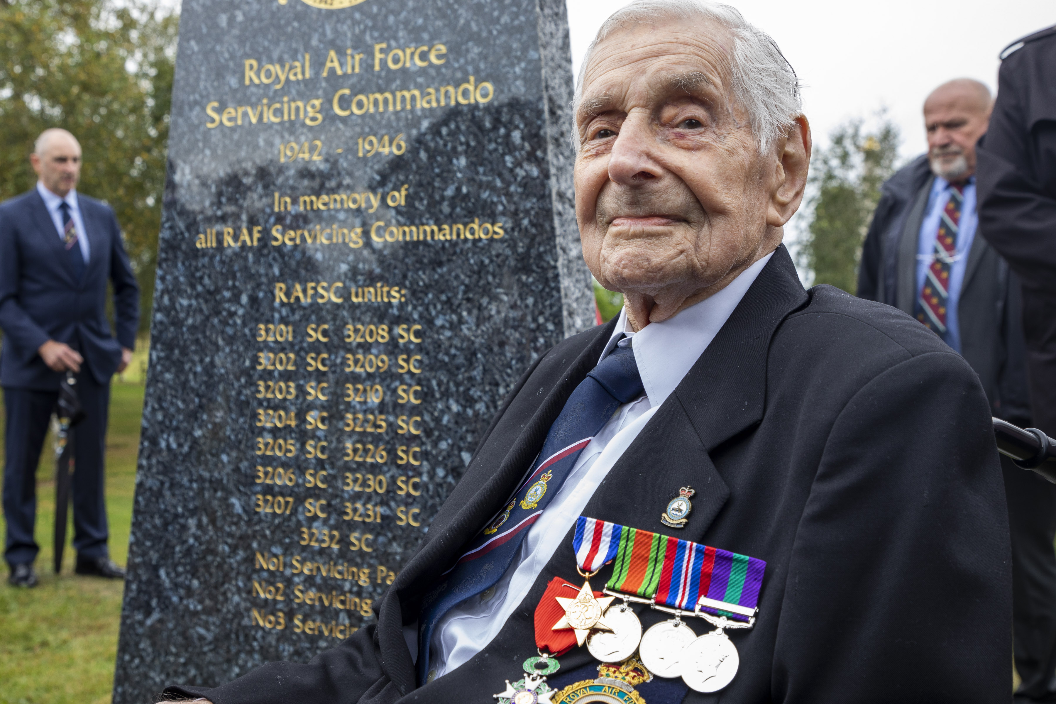 Veteran sits in wheelchair next to memorial stone.
