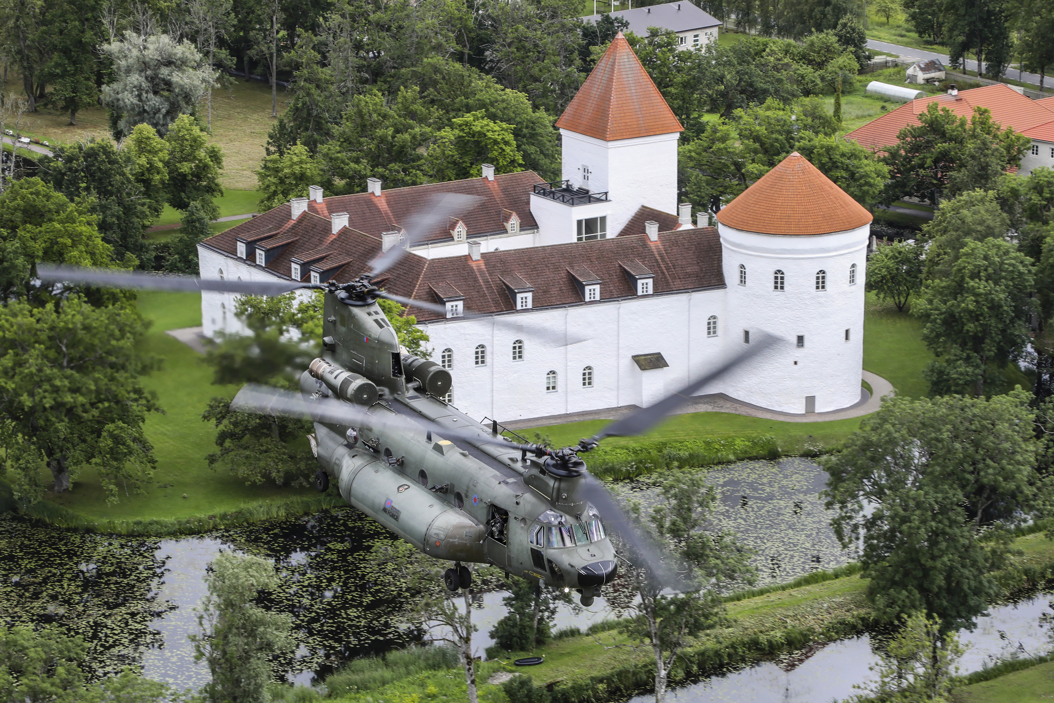 Image shows Chinook.flying over lake by white manor house.