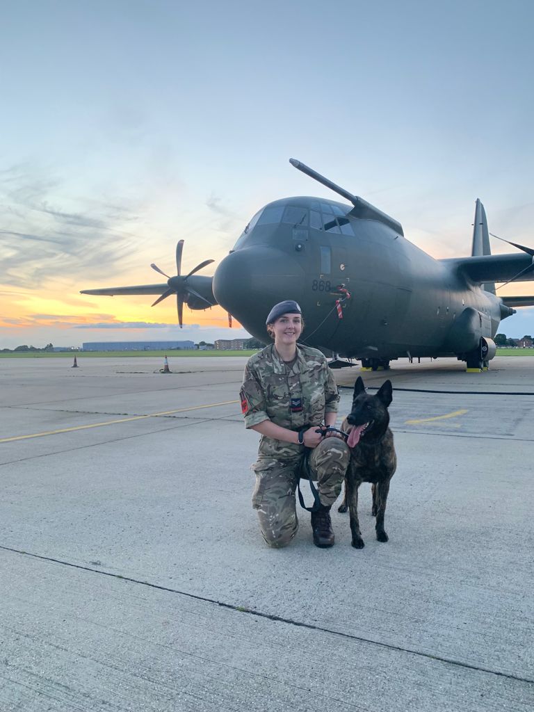 RAF Police Handler and dog with Hercules aircraft in background.
