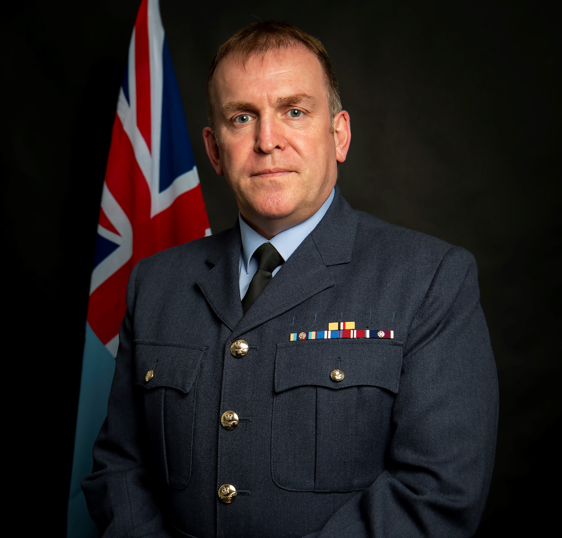 Image shows official portrait of RAF aviator with union jack flag. 