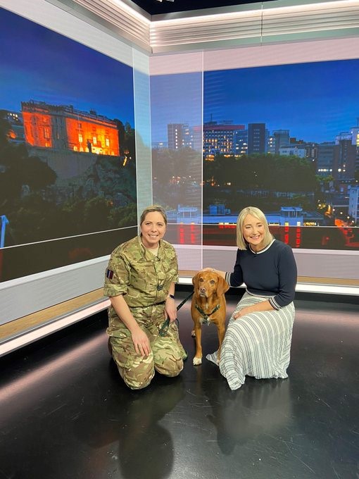 Image shows RAF personnel with her dog and a news presenter. 