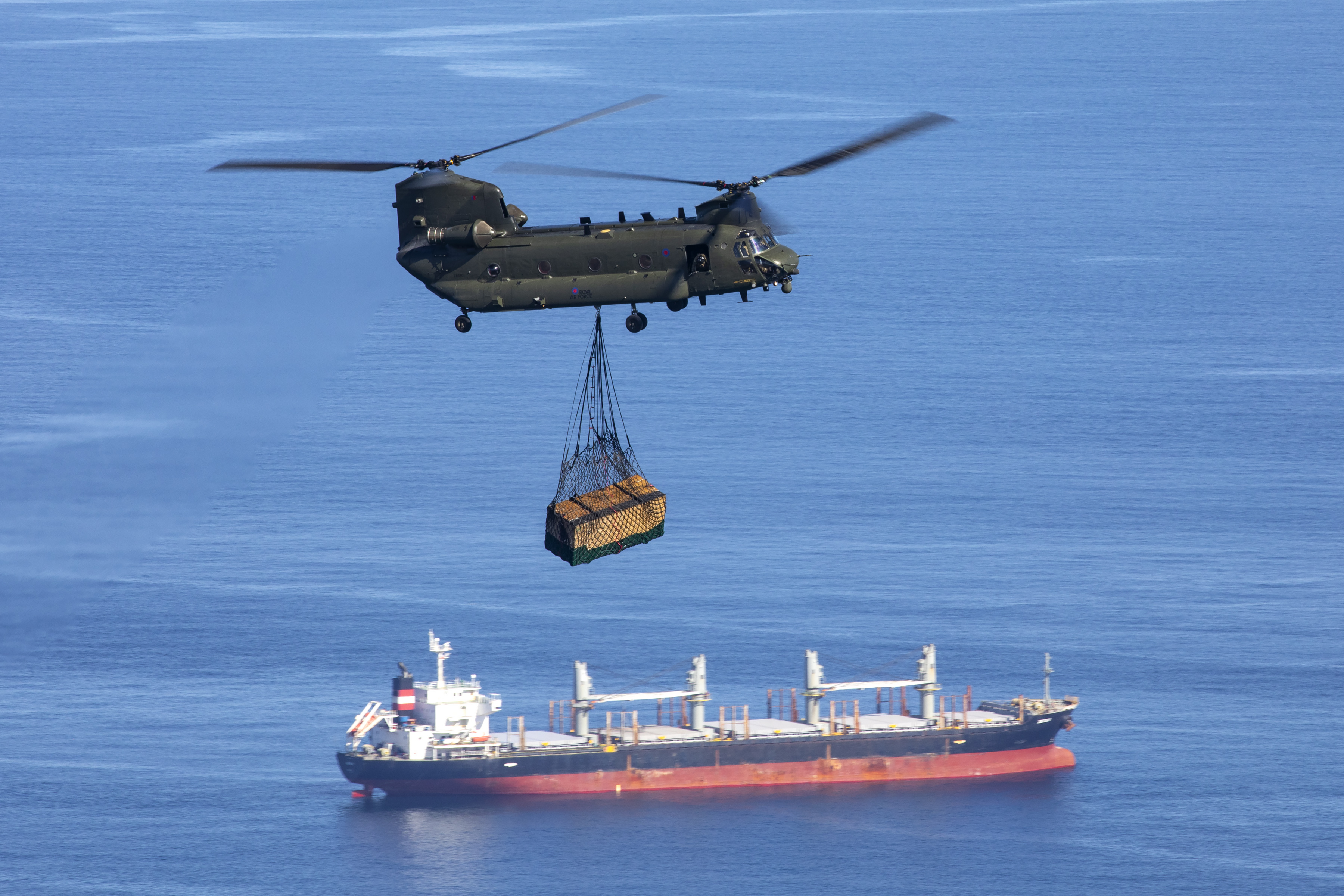 Chinook carries loaded sling over cargo ship.