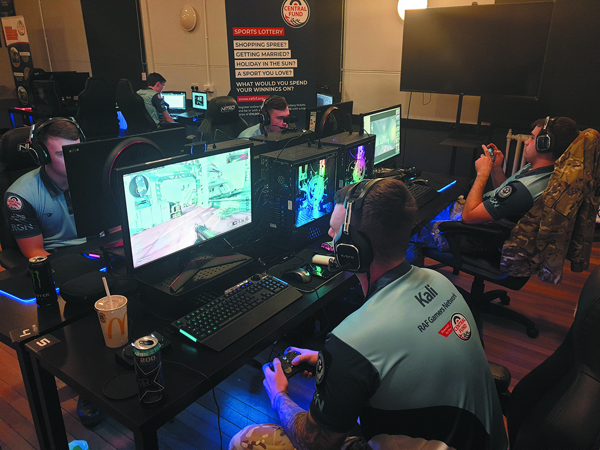 Personnel sit at computers gaming and wearing headphones.