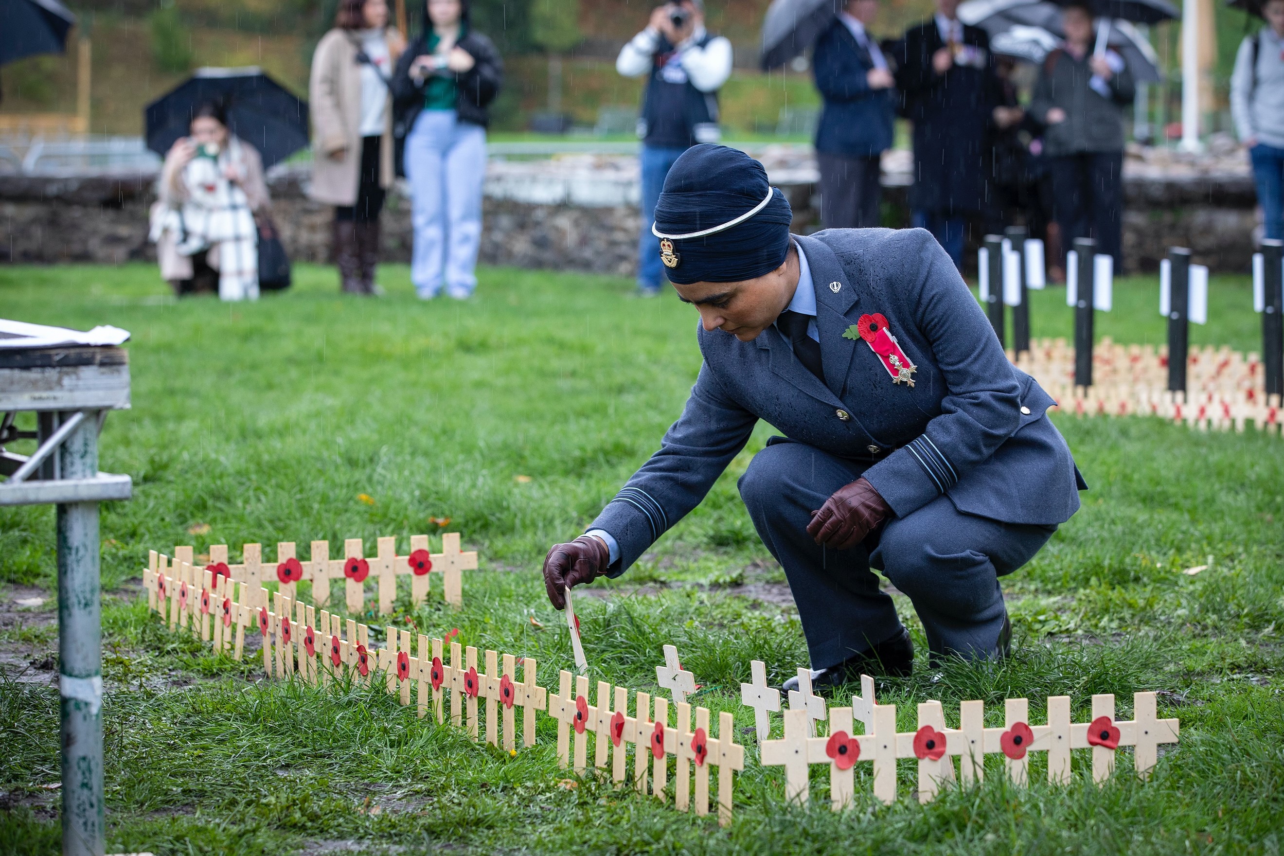 Image shows RAF aviator placing a poppy cross in cemetery.