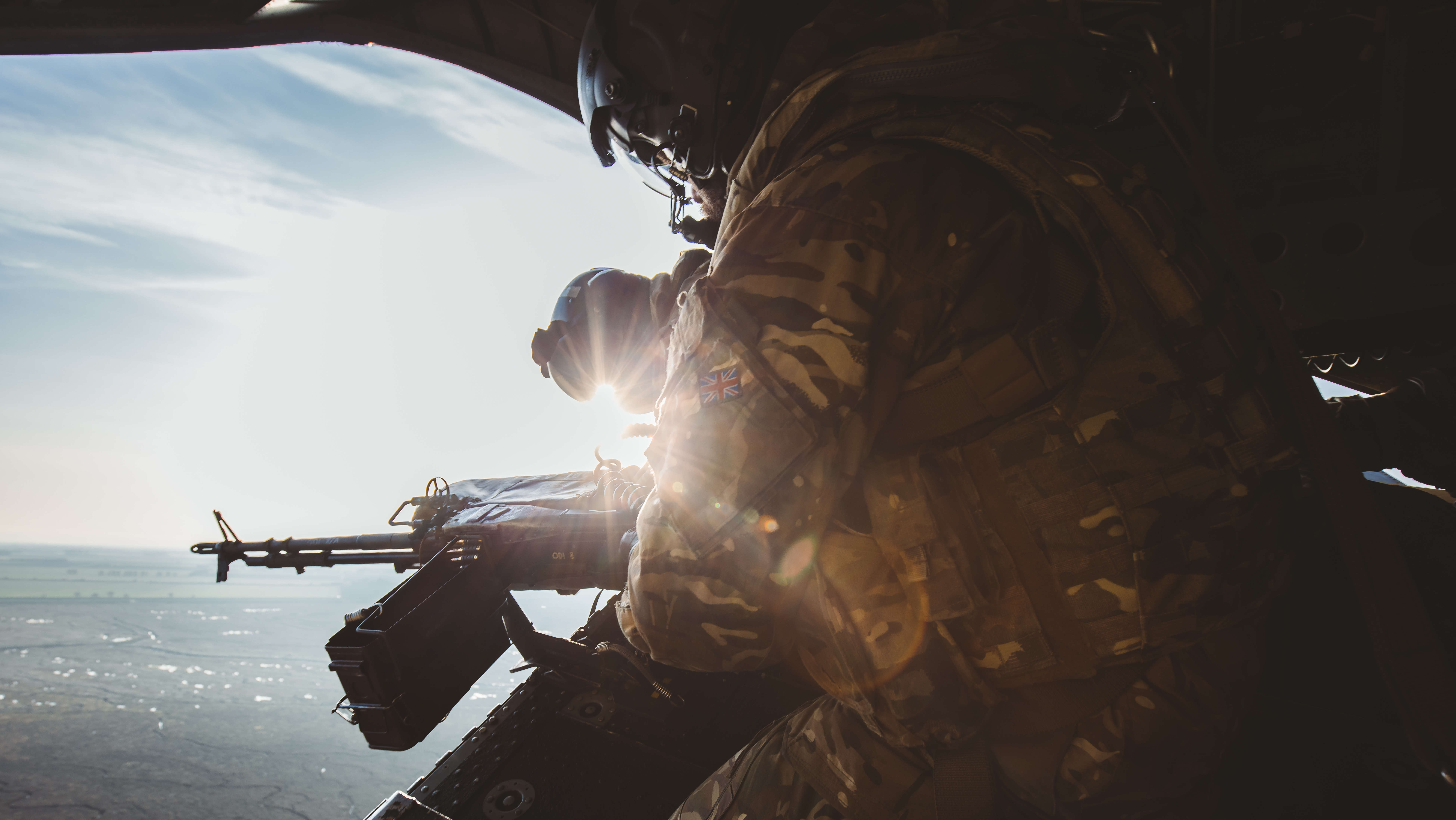 Image shows RAF Gunner manning machine gun from the back of a Chinook while it is in flight.