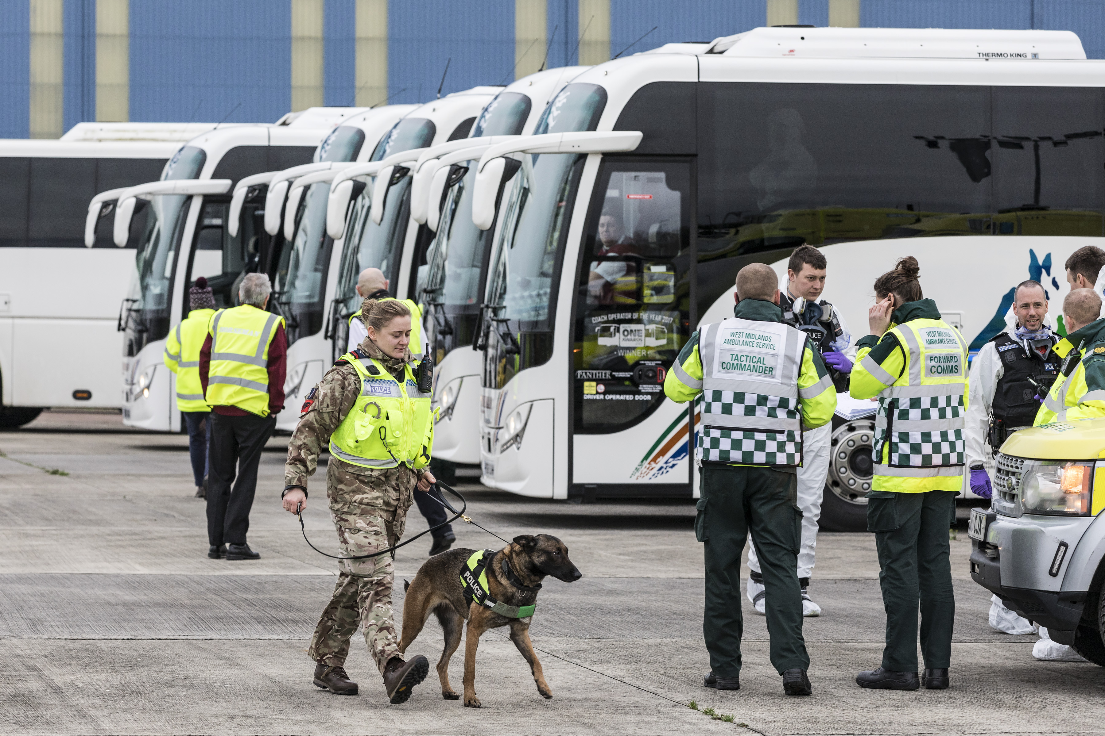 RAF Police walks dog around coaches and emergency personnel and vehicles.