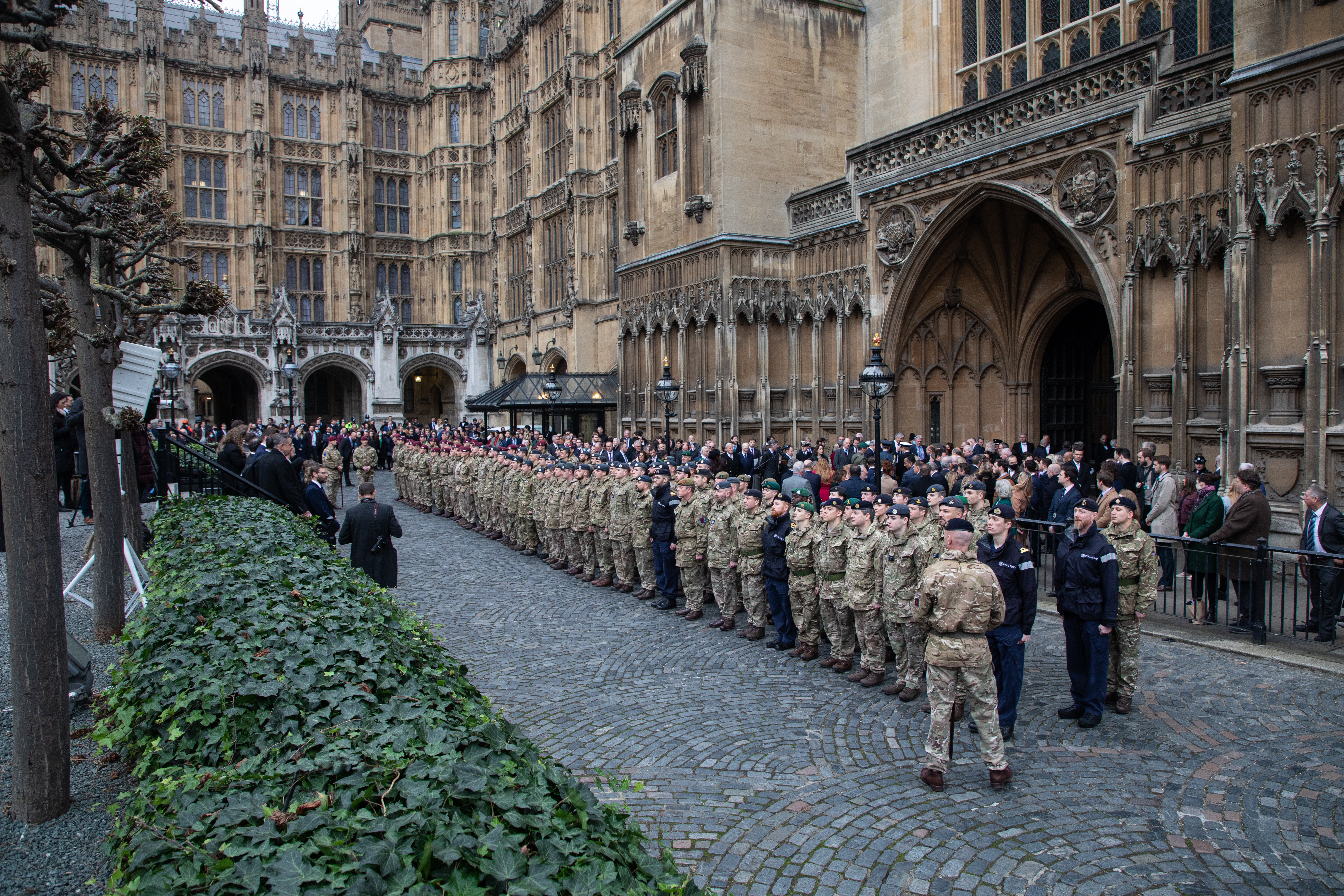 Armed Forces stand outside Parliament with Prime Minister and other notable figures.