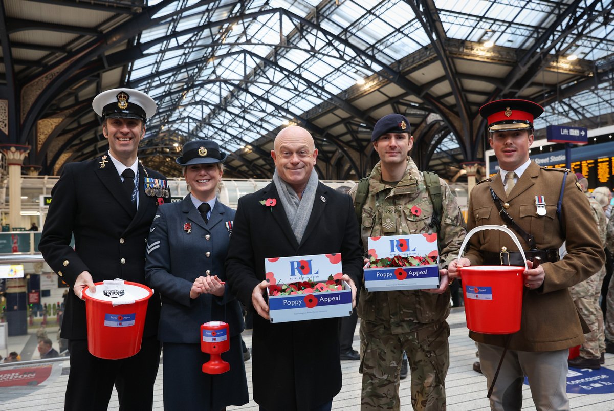 Personnel stand in a train station with Poppy bucket collections and Ross Kemp.