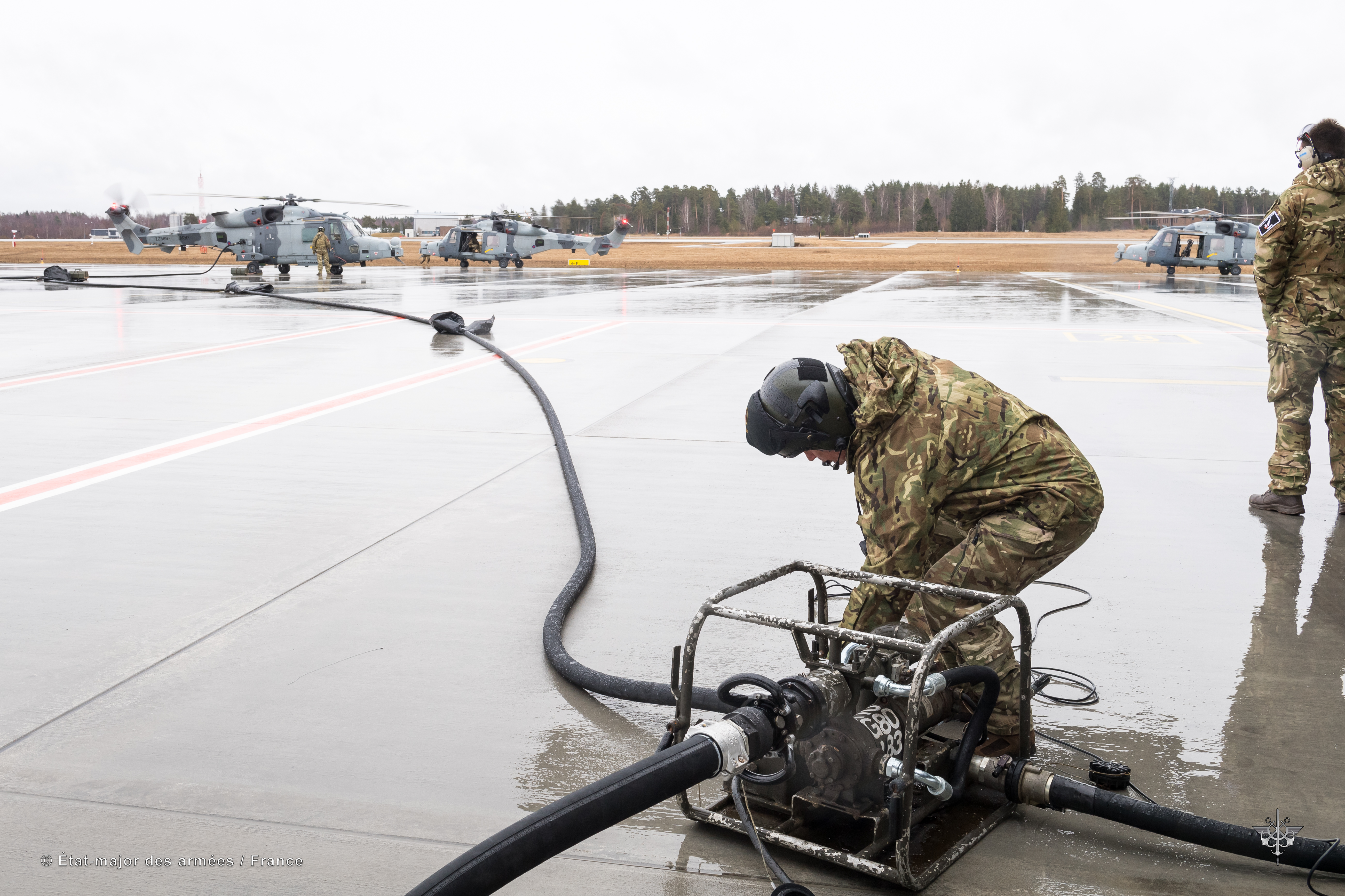 Pilot tends to refuelling pump with two helicopters on airfield.