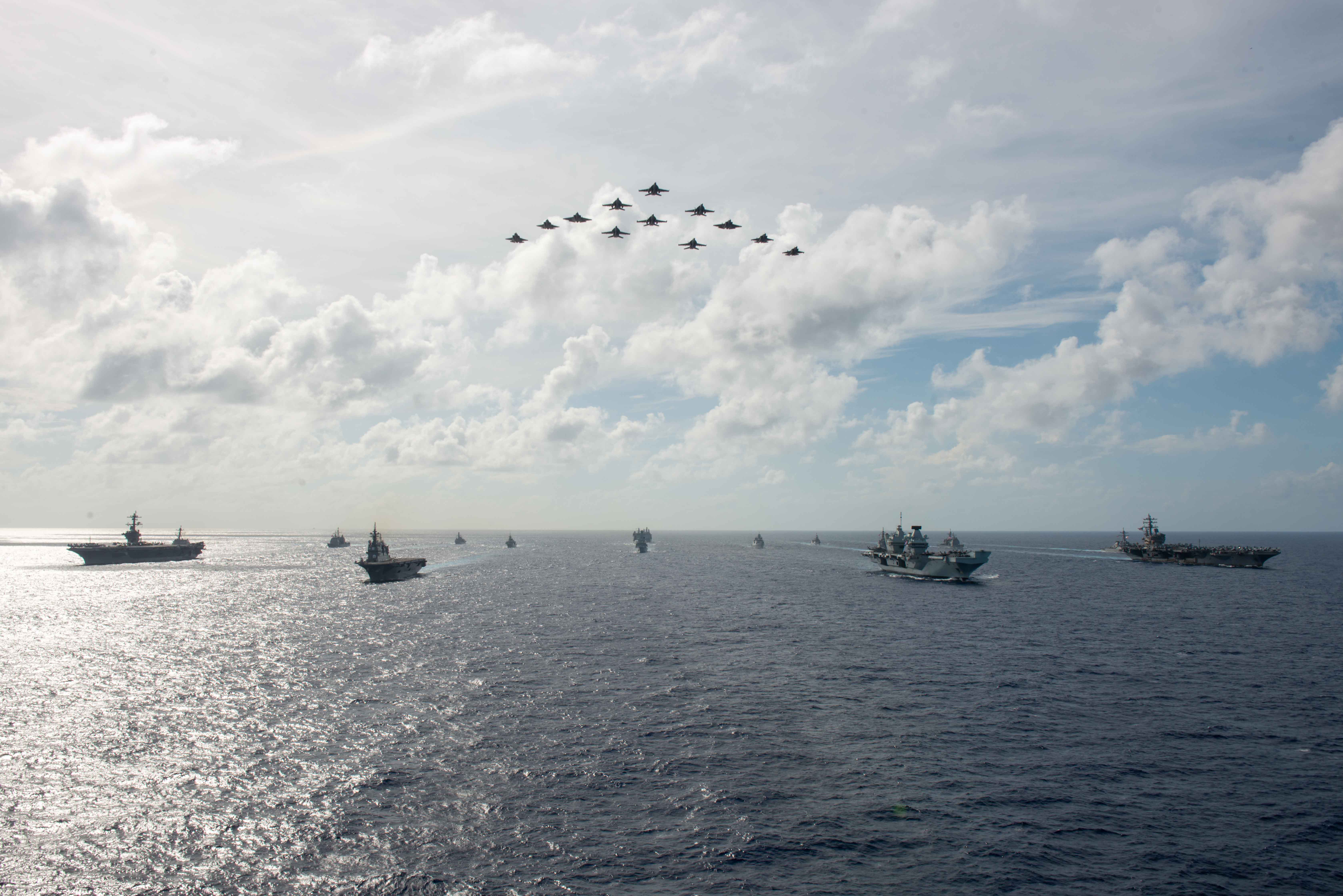 Two F-35B Lightnings fly in formation over Aircraft carriers.