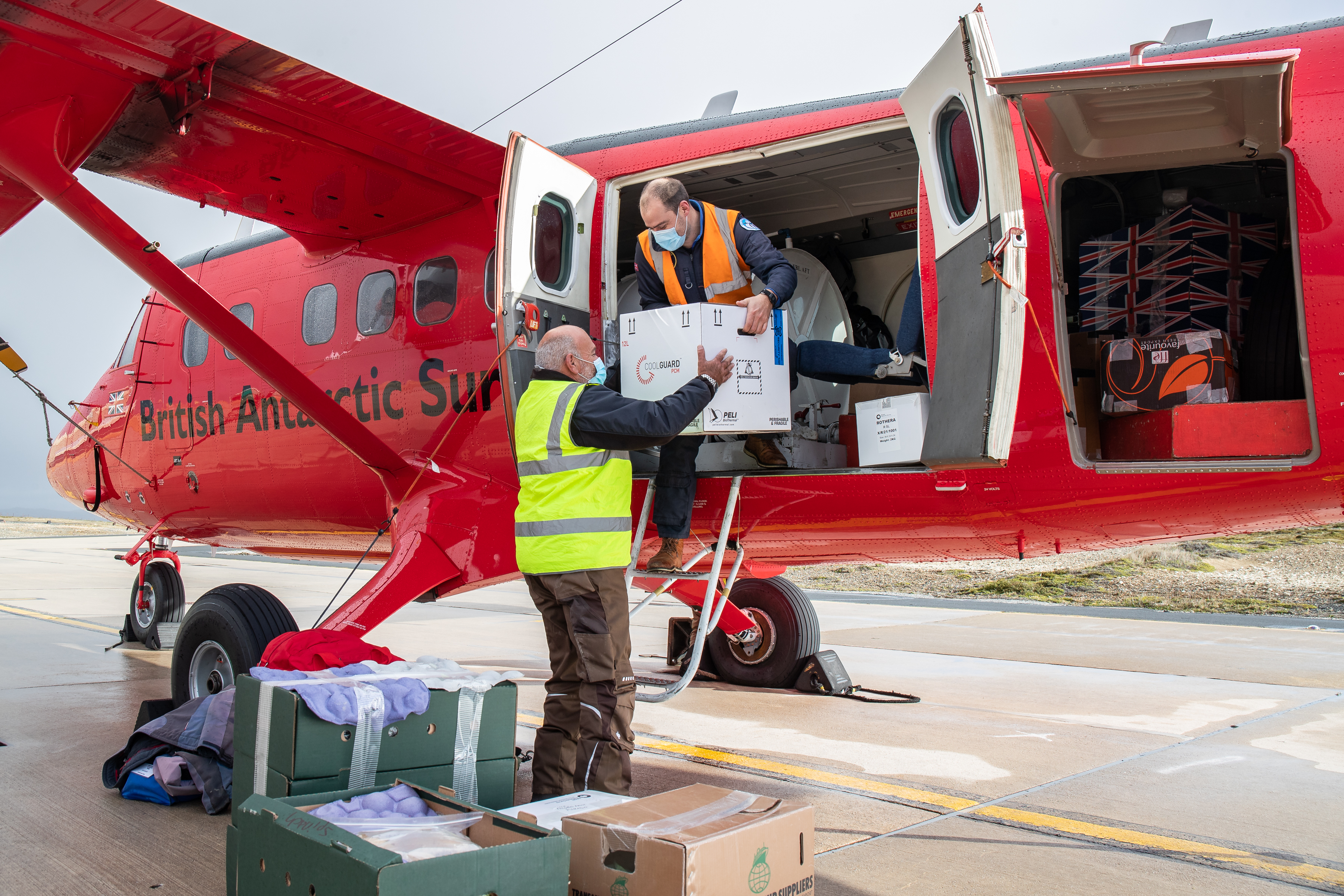 Boxes are loaded onto red plane labelled the British Antarctic Survey. 