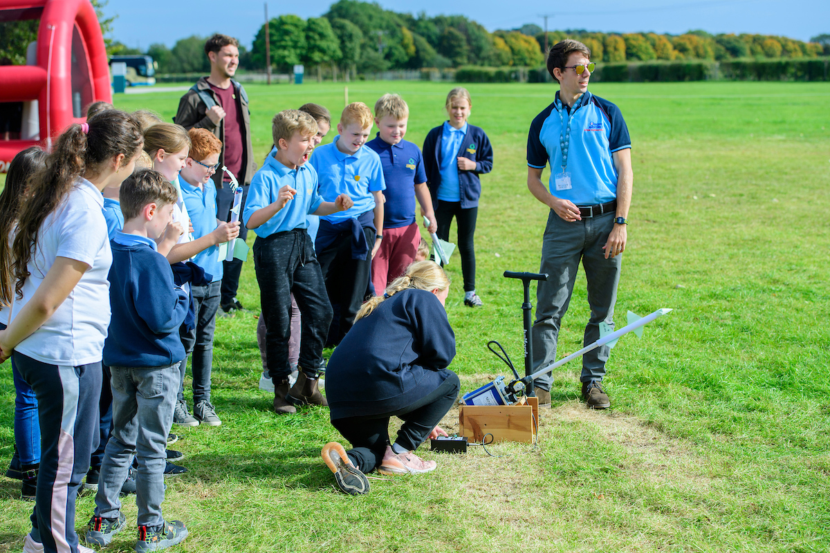 Image shows RAF STEM ambassador with school children outdoors.