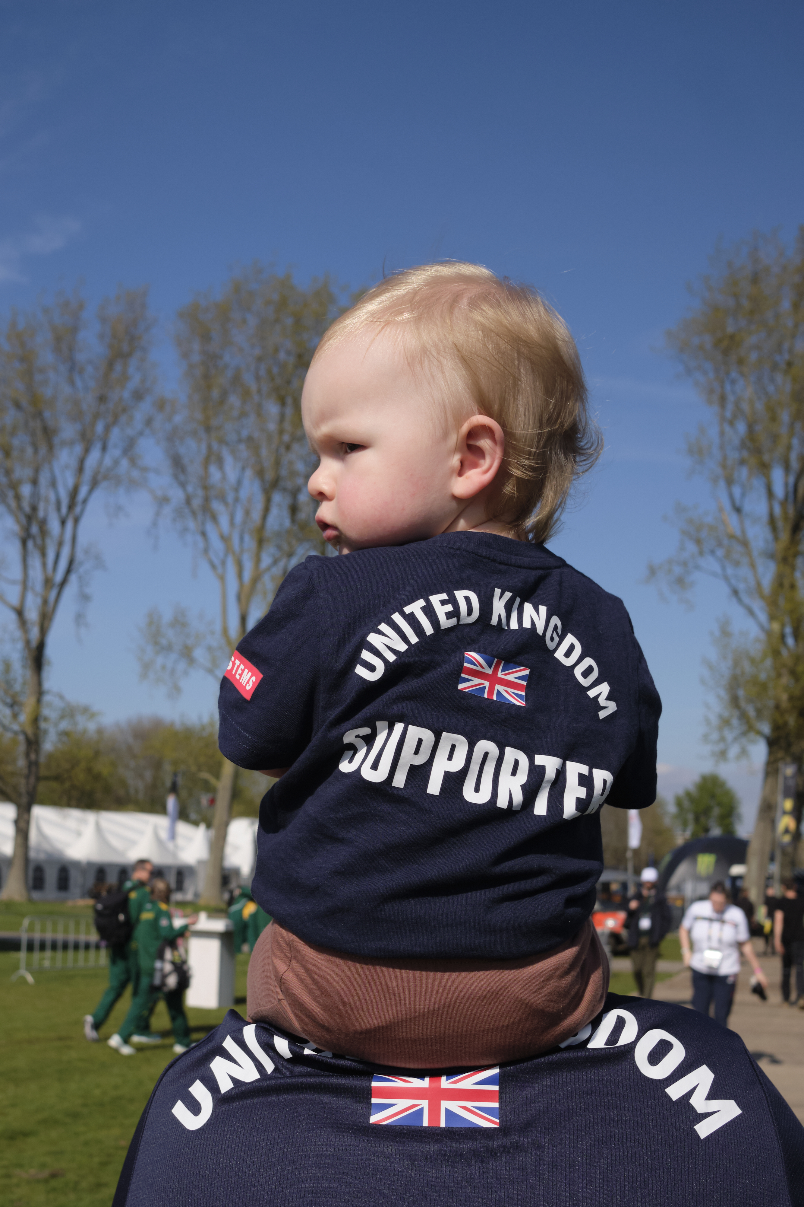 Toddler sits on fathers shoulders, while wearing UK supporter t-shirt.