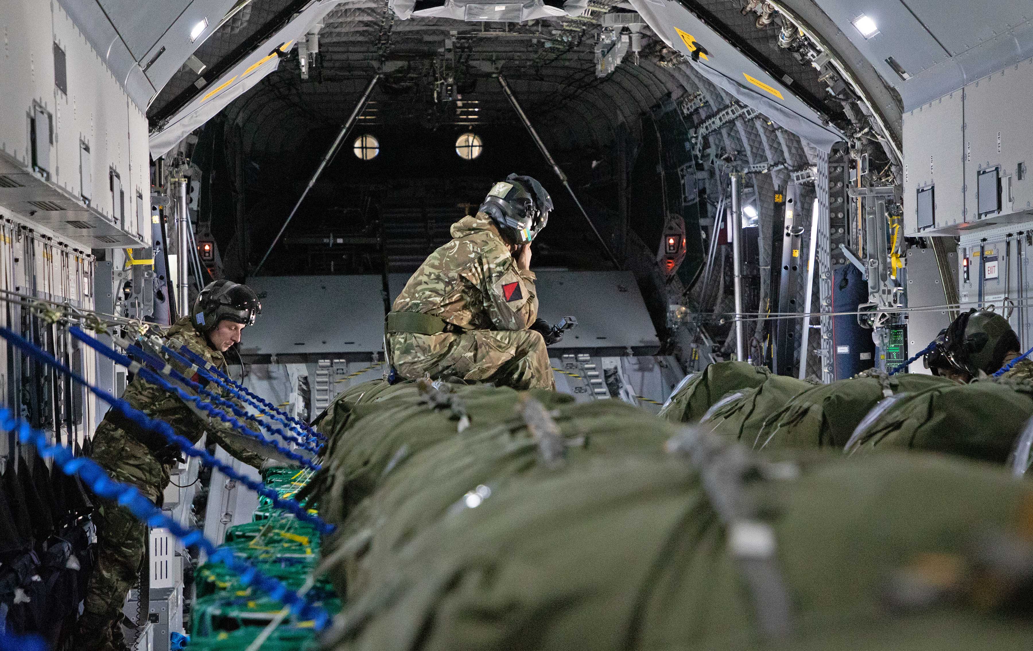 Image shows RAF aviators sitting on cargo inside holding bay of carrier aircraft.