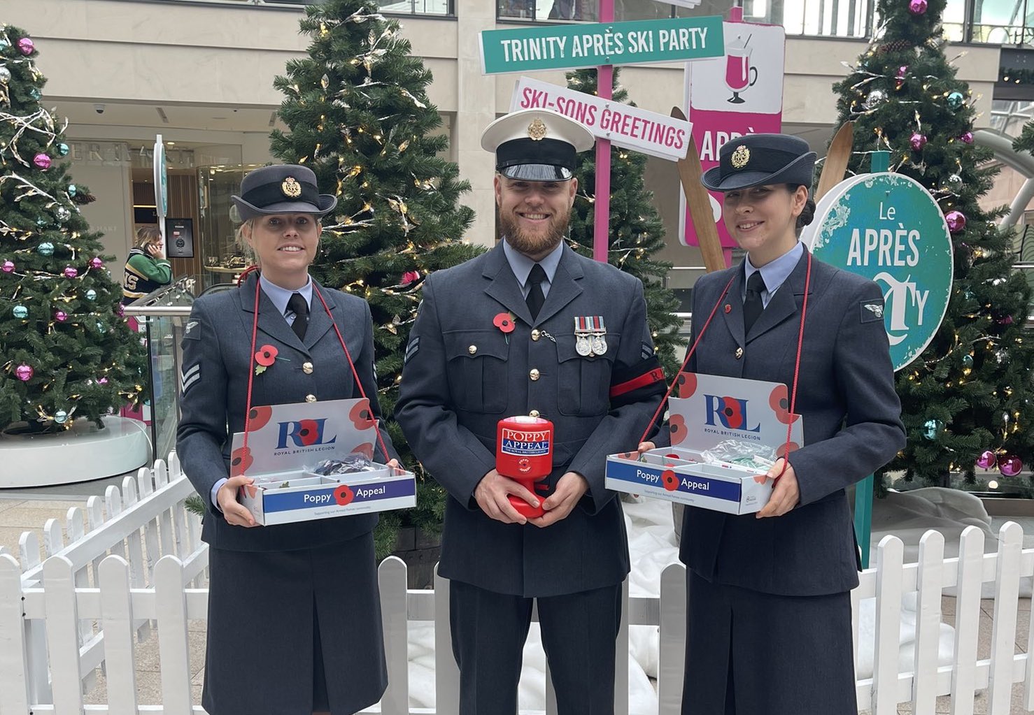 Personnel stand by Christmas trees in a shopping centre, with Poppy bucket collections. 