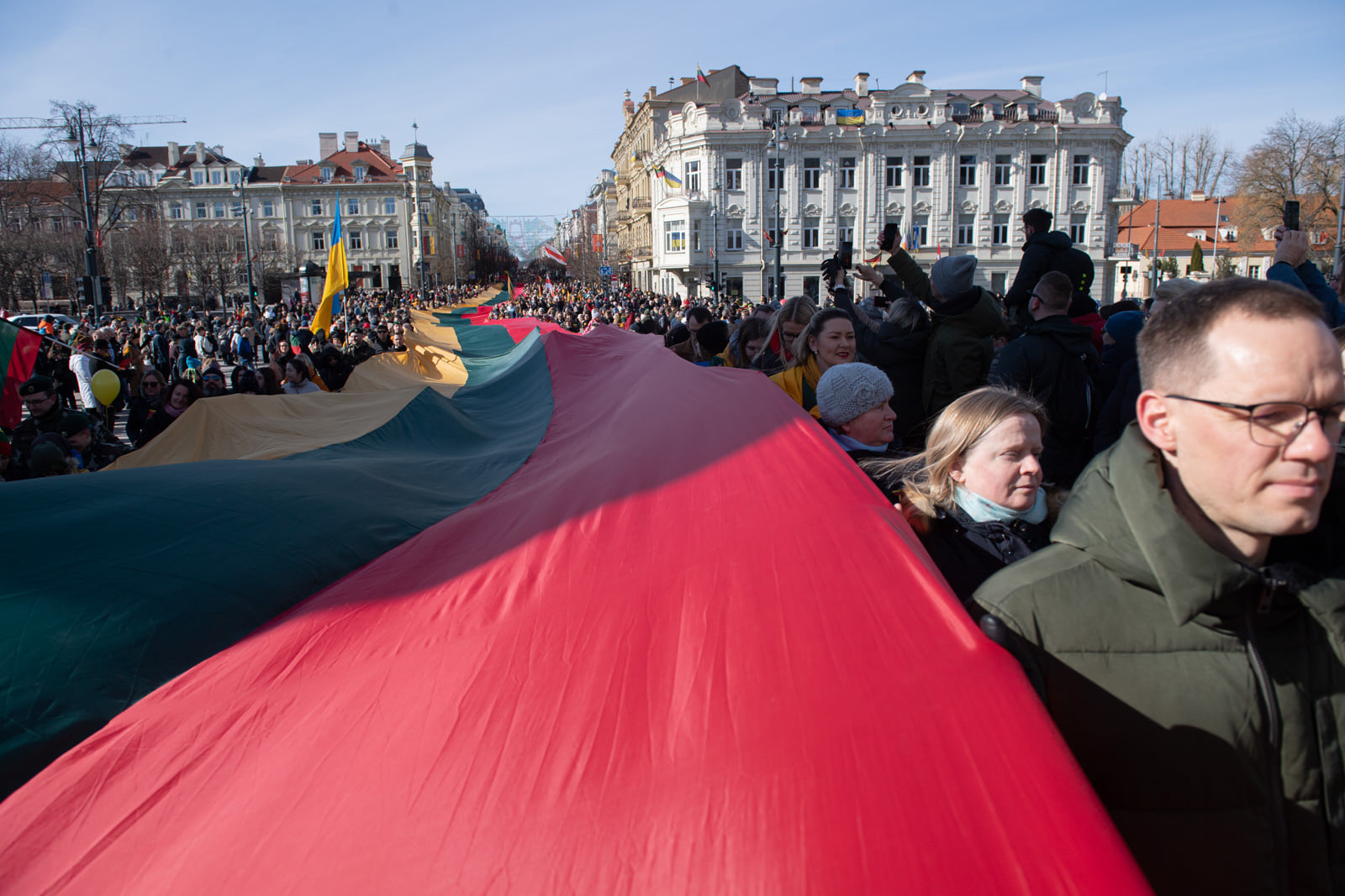 Flag of Lithuania held between crowd of people.