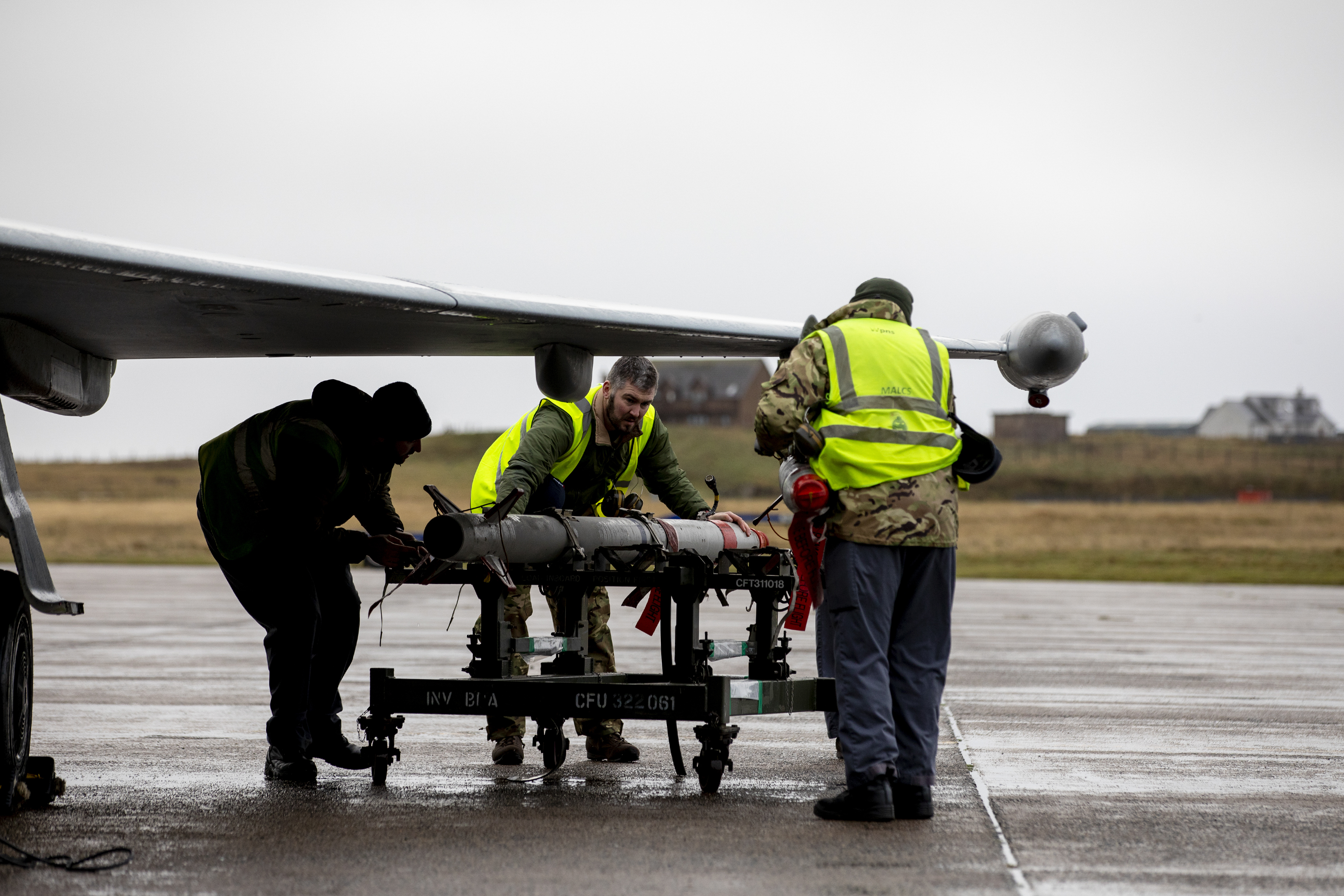 Personnel move missile under Typhoon wing, on the runway.