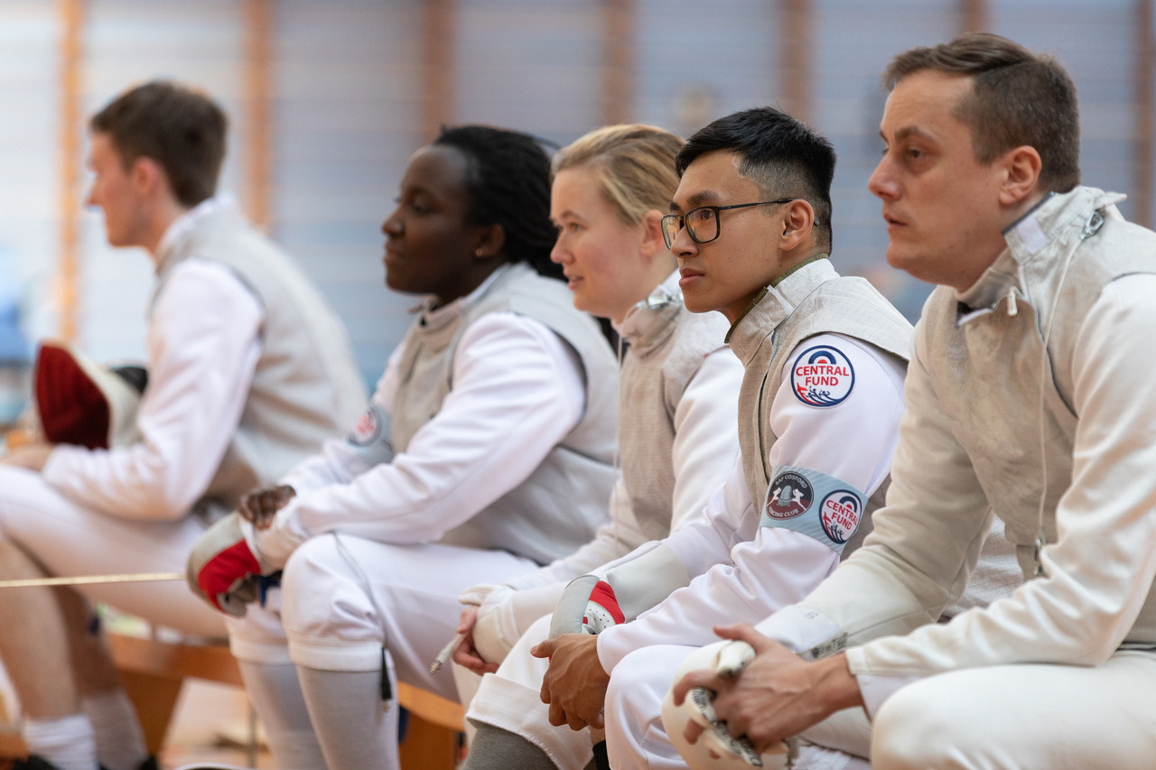 Personnel sit in fencing outfits.