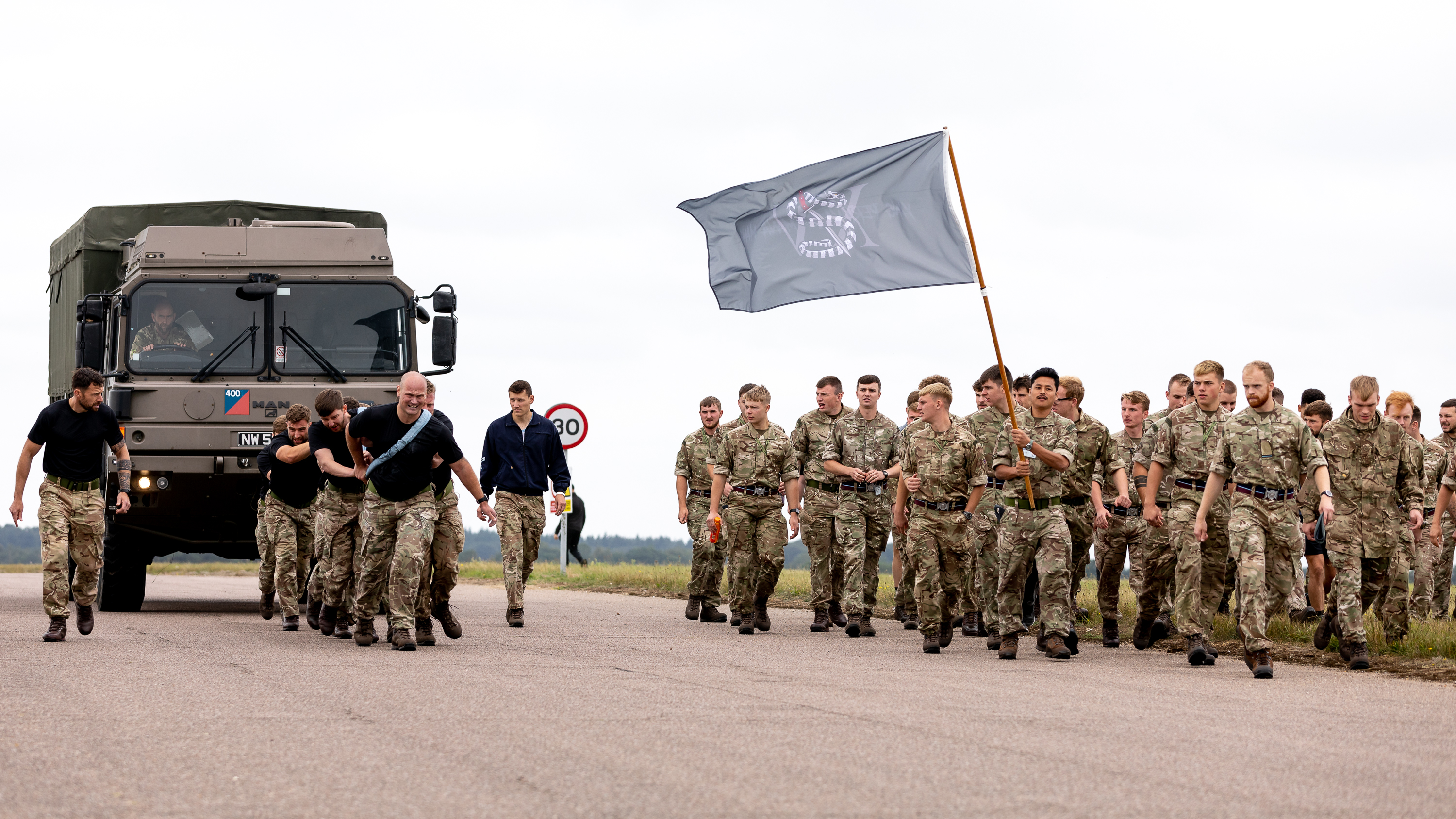 Personnel with 15 Squadron RAF Regiment flag walk alongside personnel pulling a vehicle.