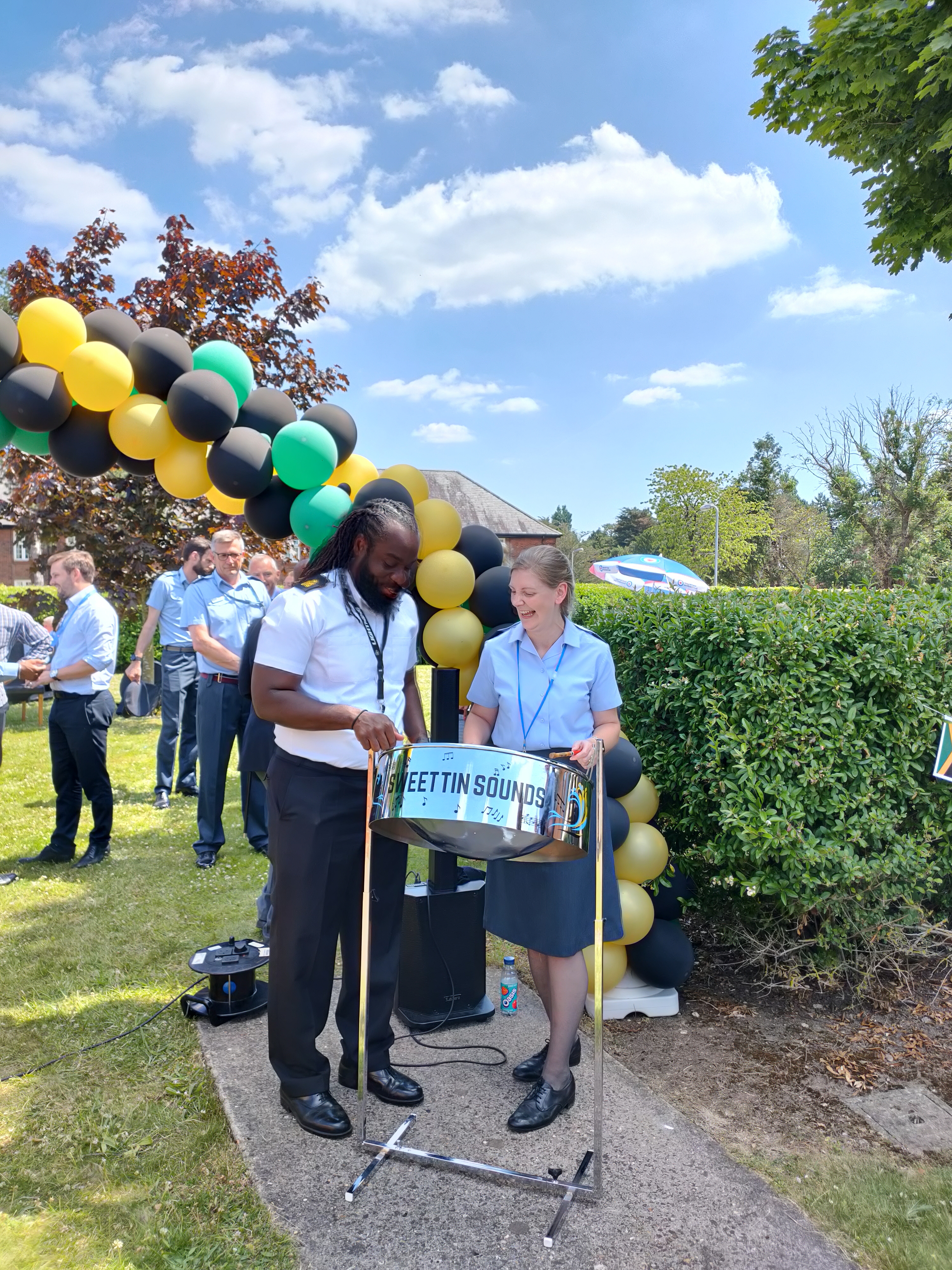 Aviators play steel drum by arc of balloons in the colours of the Jamaican flag.