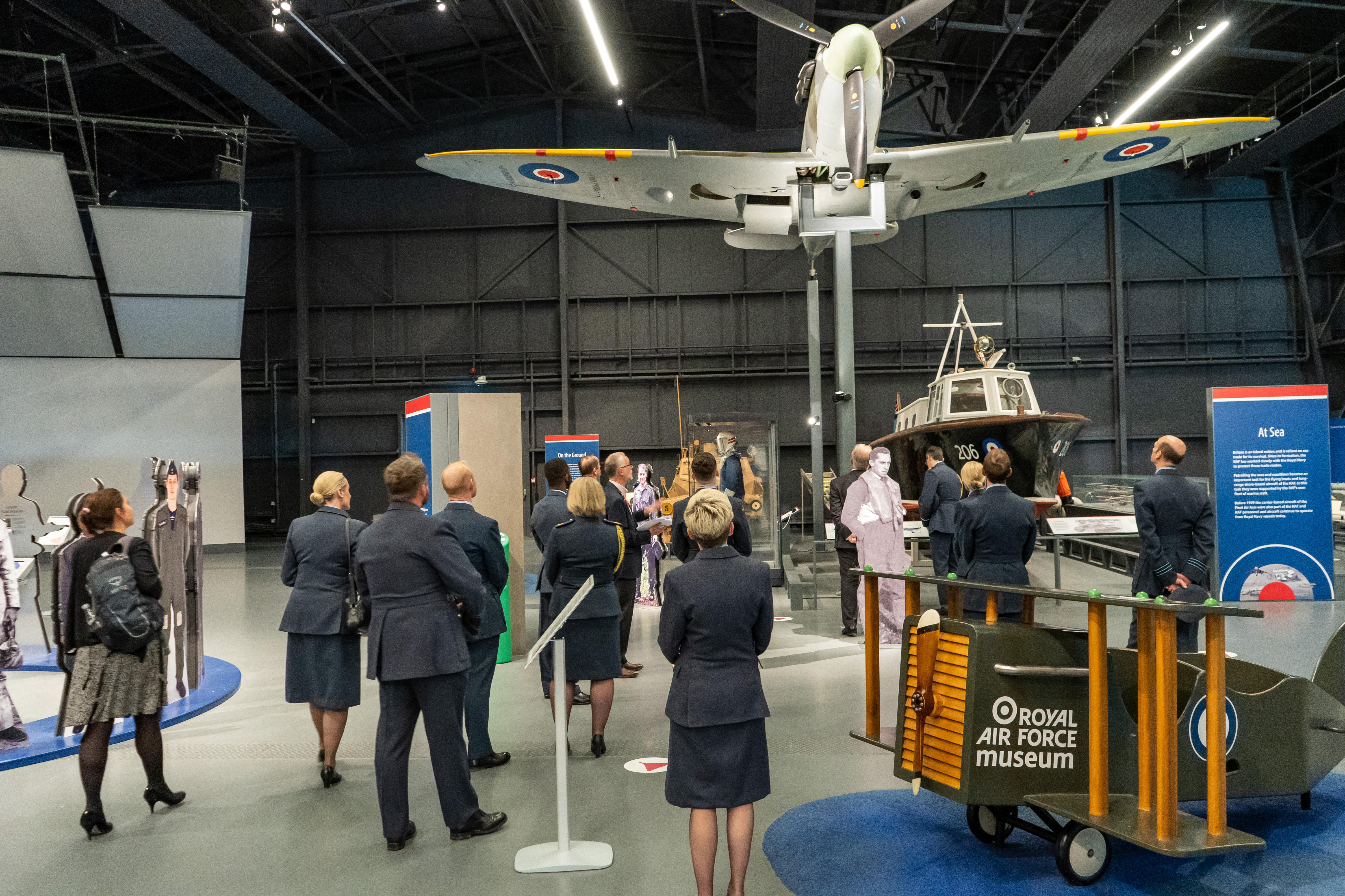 Personnel in museum under a Spitfire model exhibit.