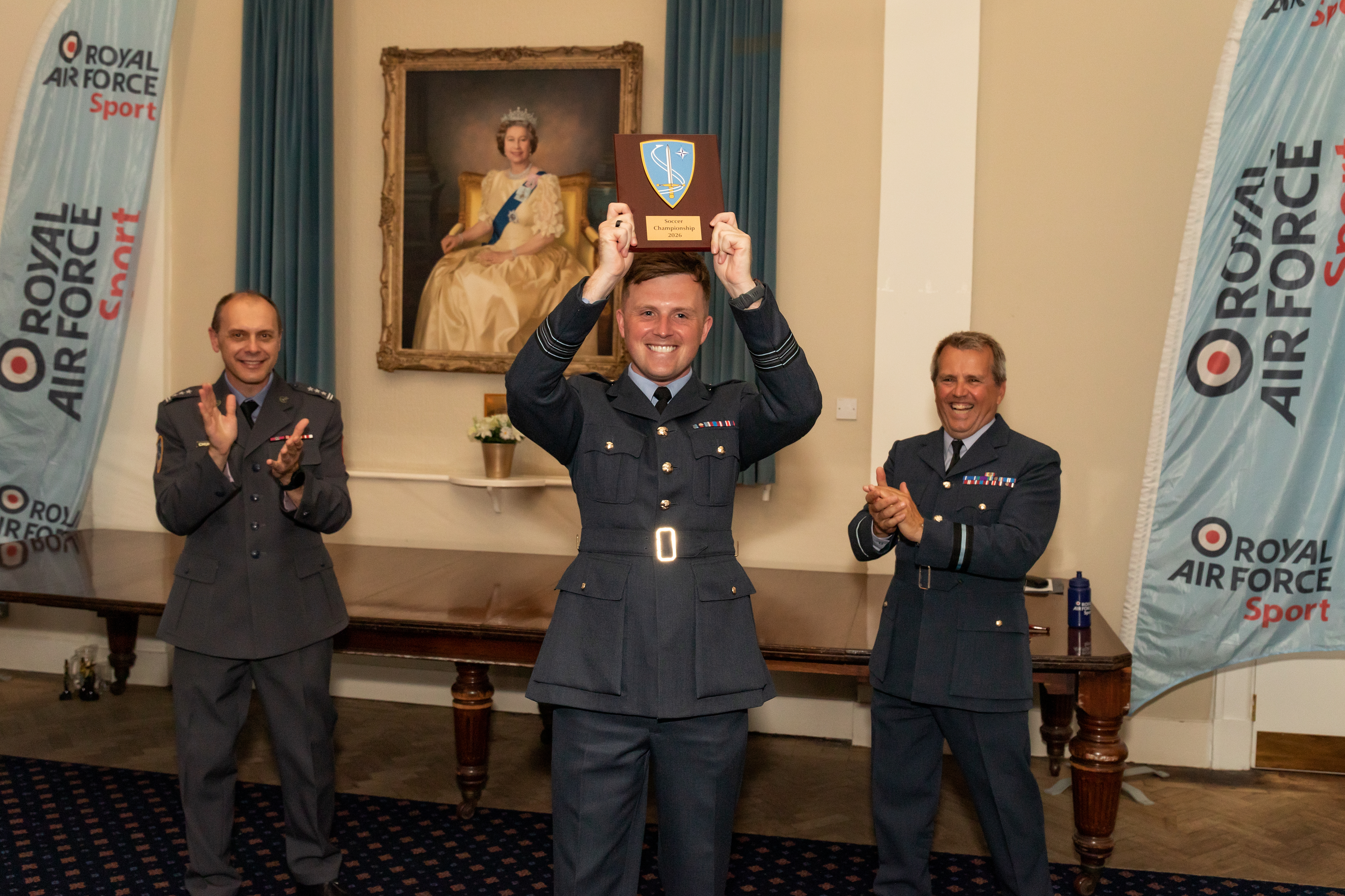 An RAF service person holding a Soccer Championship 2026 plaque in the air.