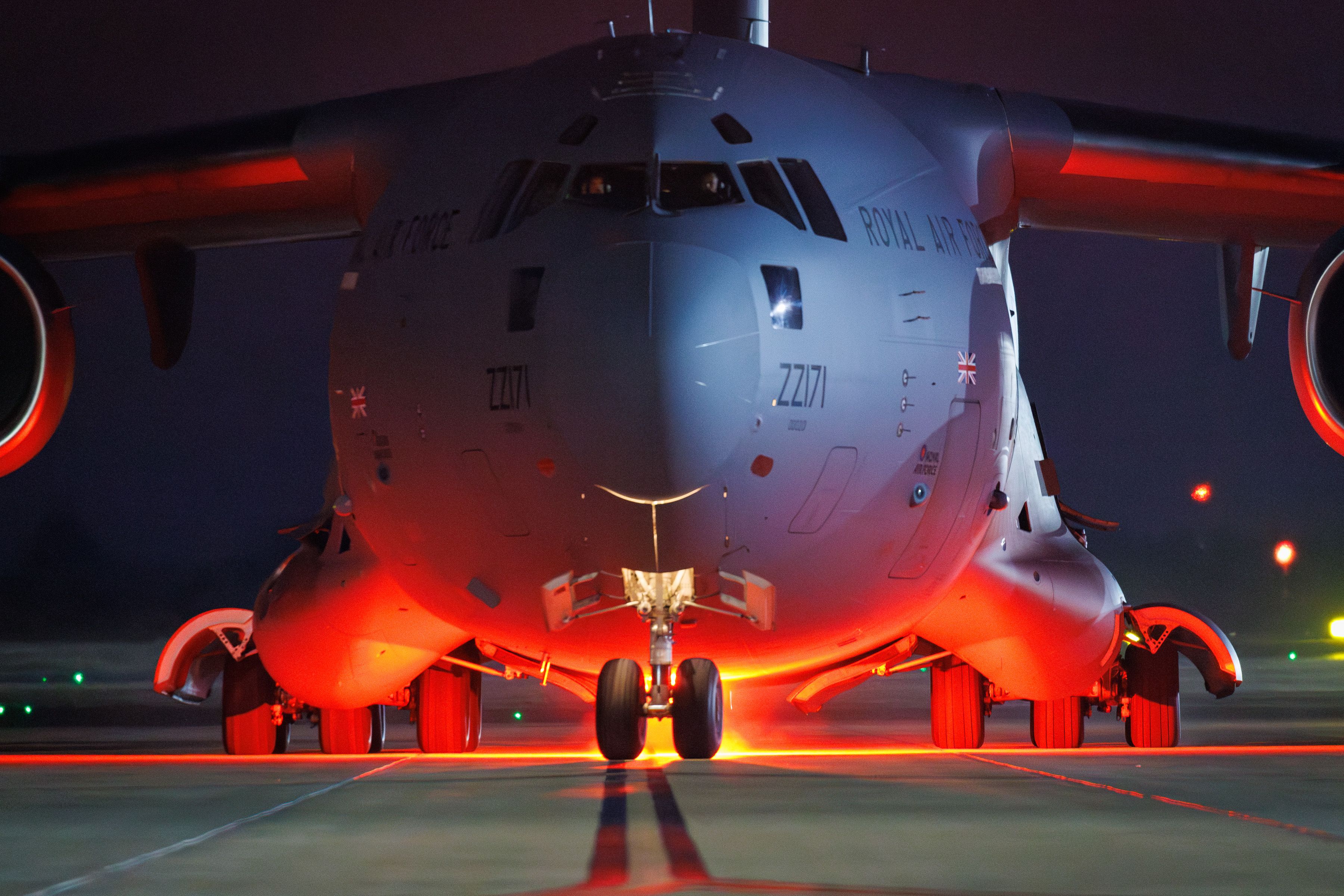 Close up of C-17 aircraft on runway at night, lit up from beneath by red light