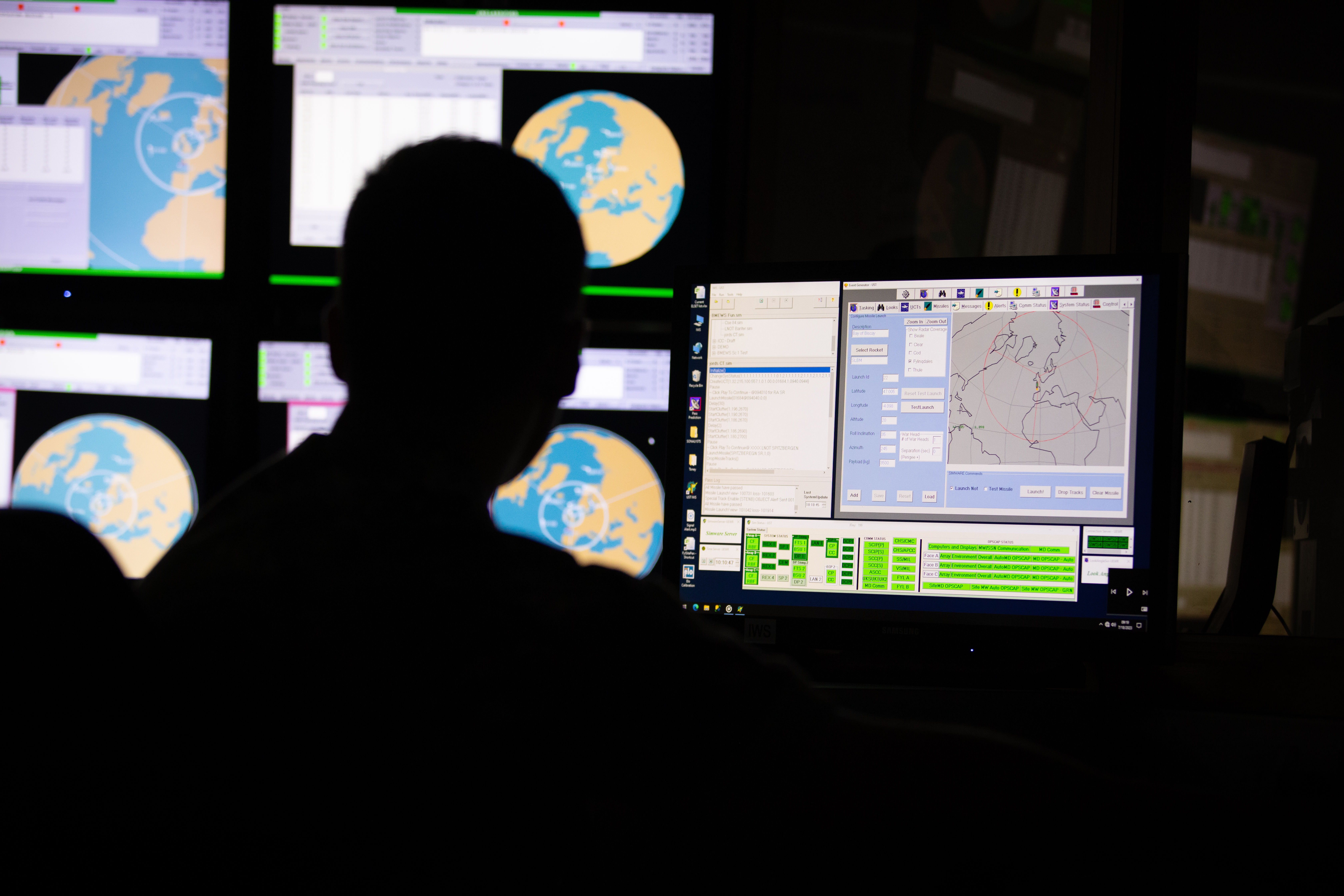 Silhouette of a man sat in front of computer screens 