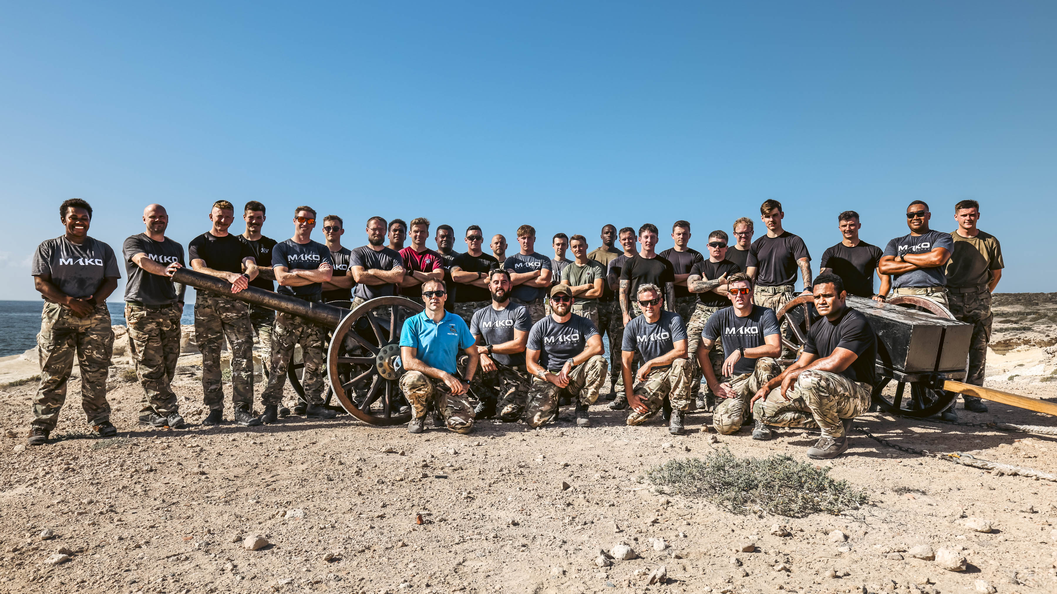 Team photo with the field gun at the top of a rugged hill with the sea in the background.