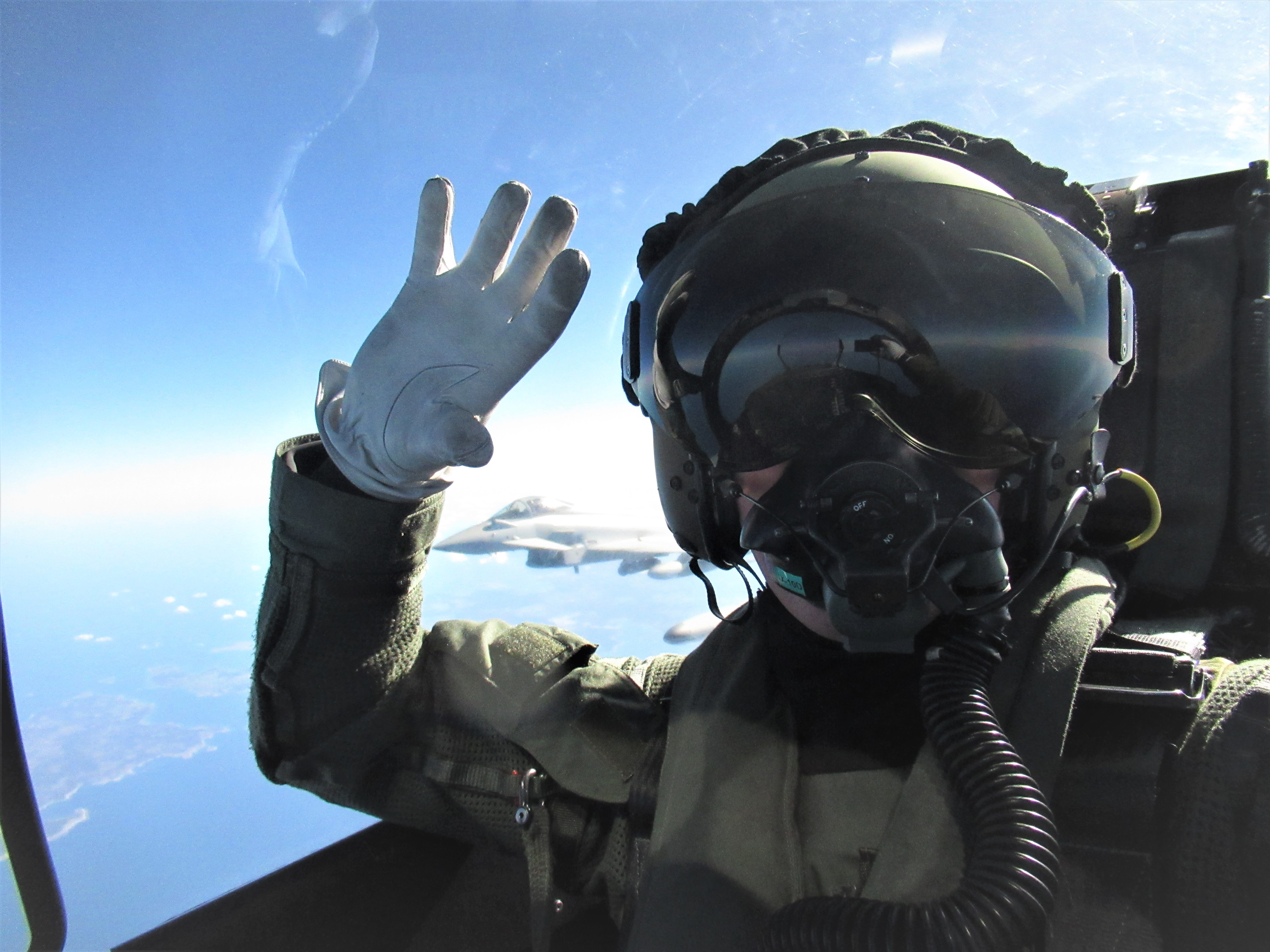 Cockpit view of pilot in aircraft waving at the camera, with another Typhoon aircraft in the background.