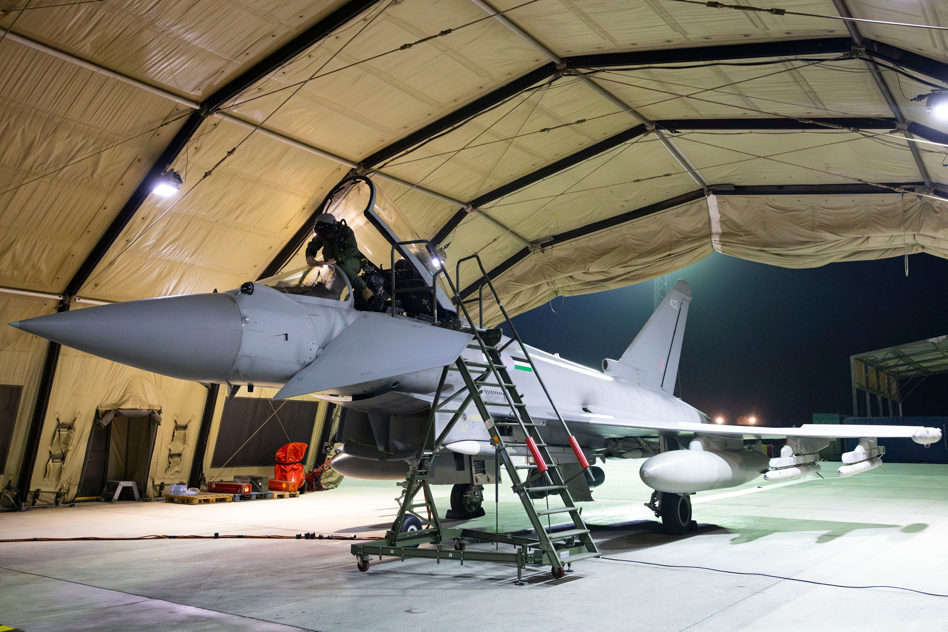 A pilot climbs into the cockpit of a 12 Sqn Typhoon covered by a rubberised shelter.