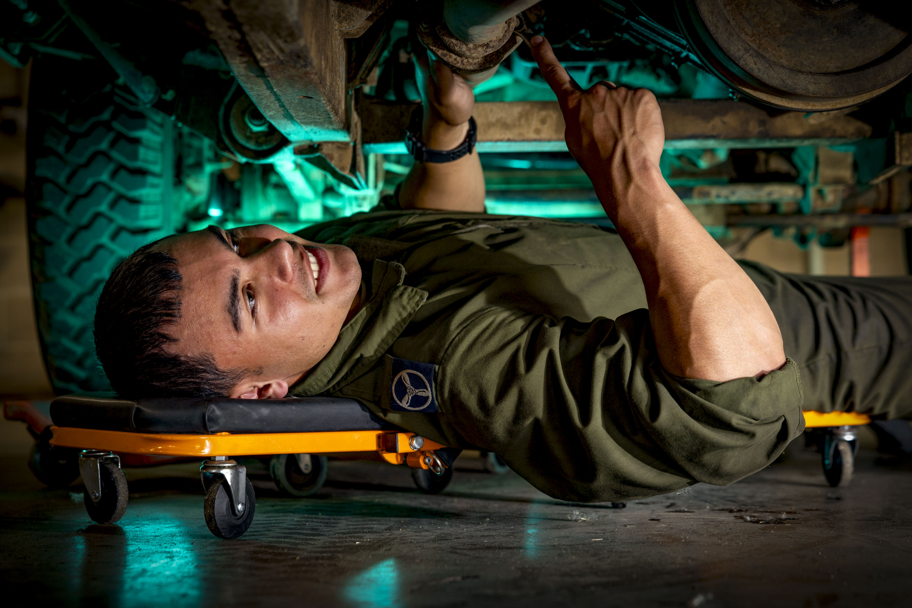 "Underneath". An Air Specialist Technician examining the underside of a vehicle. He is lying on his back, supported by a creeper.