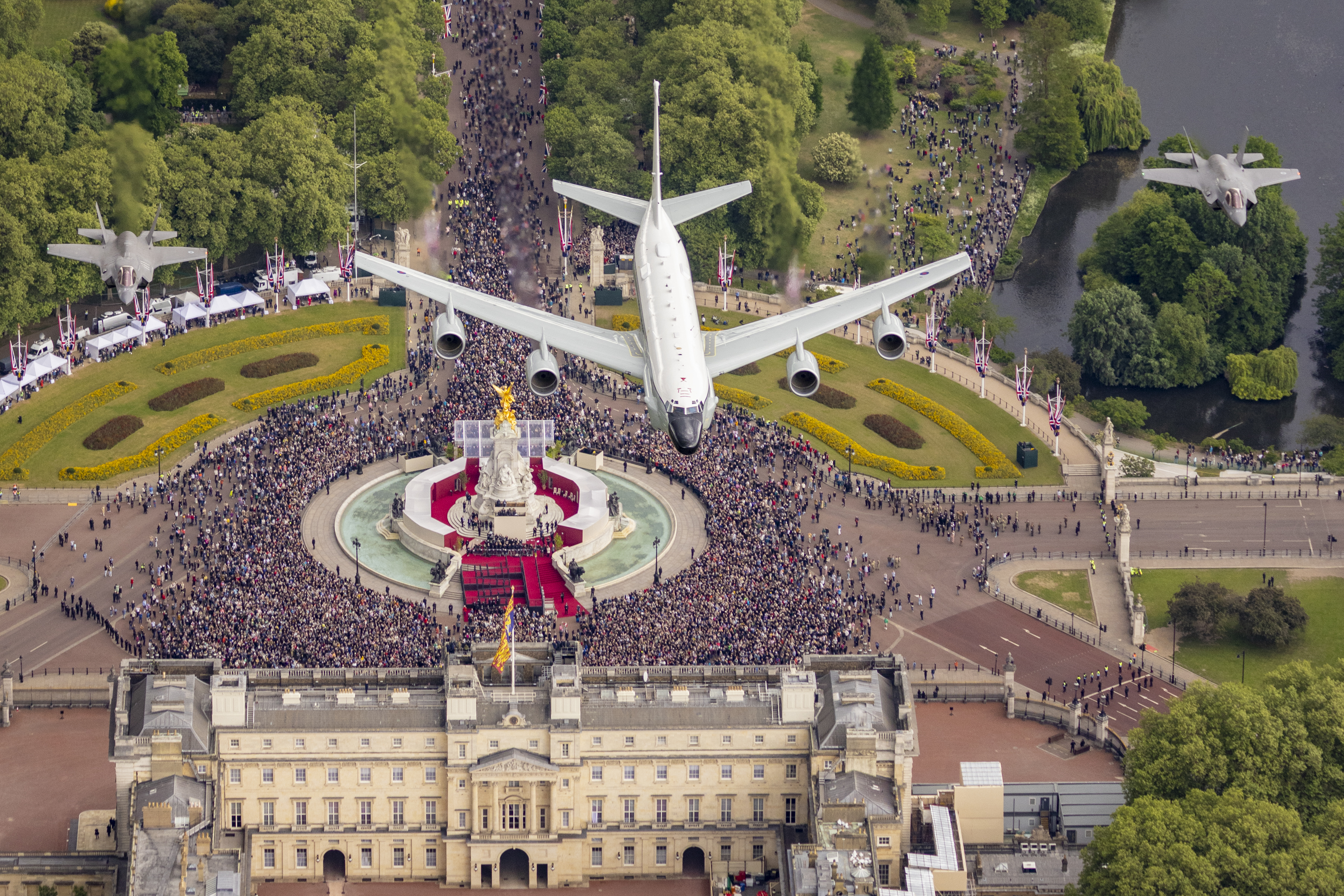 "Heroes of the Skies". A RAF RC-135W in flight over Buckingham Palace, flanked by a pair of F-35s. On the ground below, gathered crowds watch on.