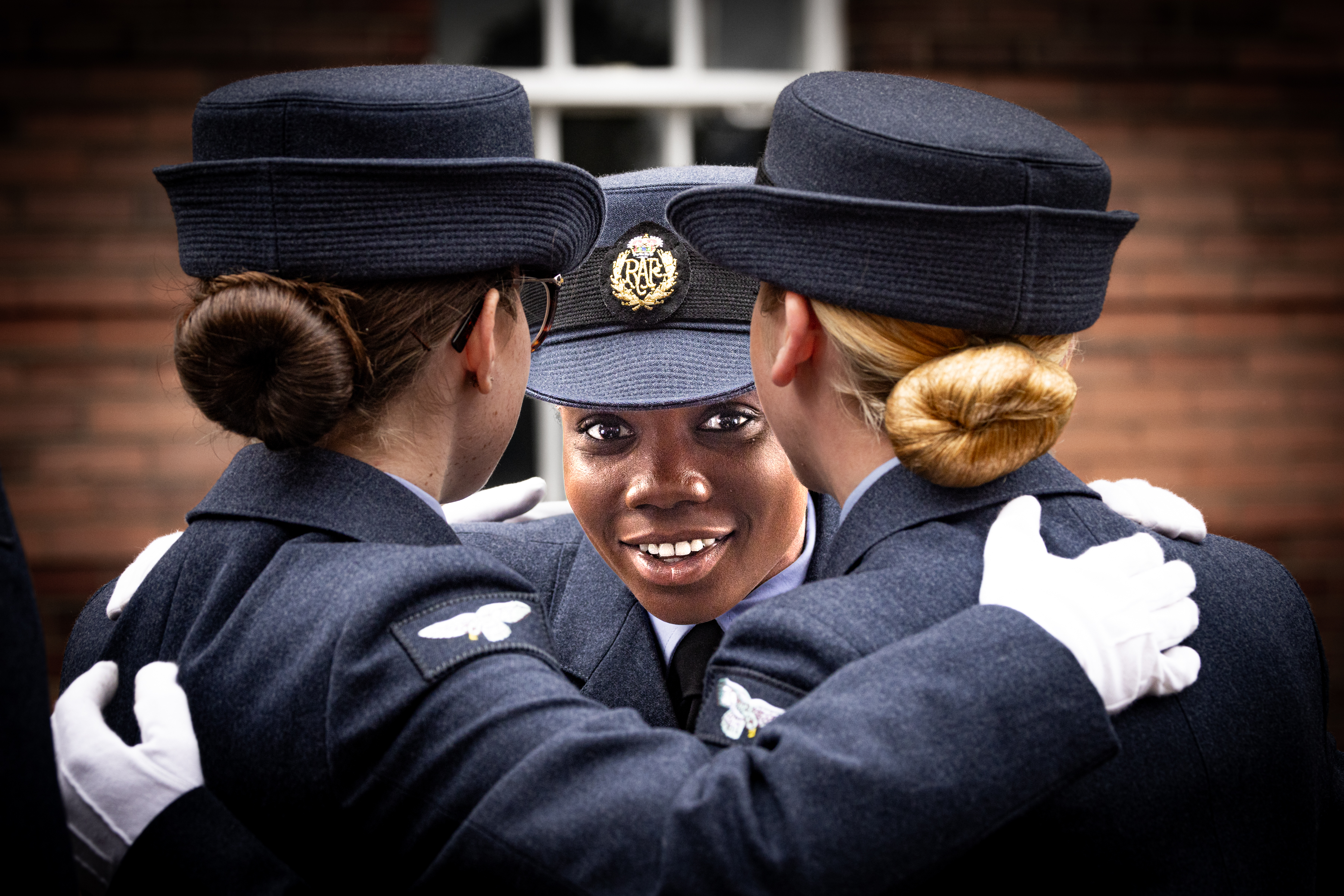 An RAF Aviator looking at the camera with her two colleagues celebrating their graduation.