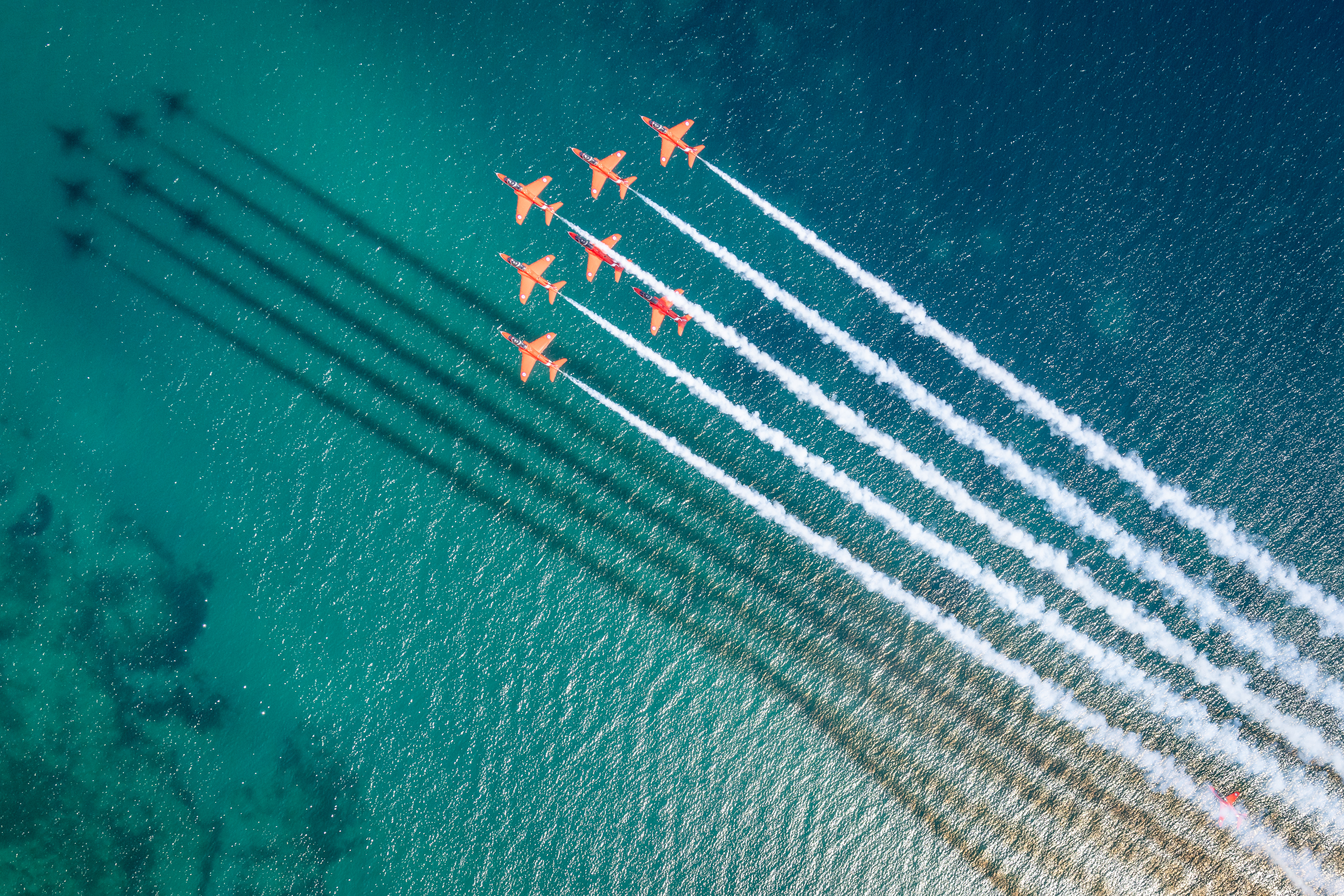 "Reflections". Seven Hawk T1s of the Red Arrows fly in formation over the sea. The shadows cast by the aircraft and their trails can be seen in the water below.