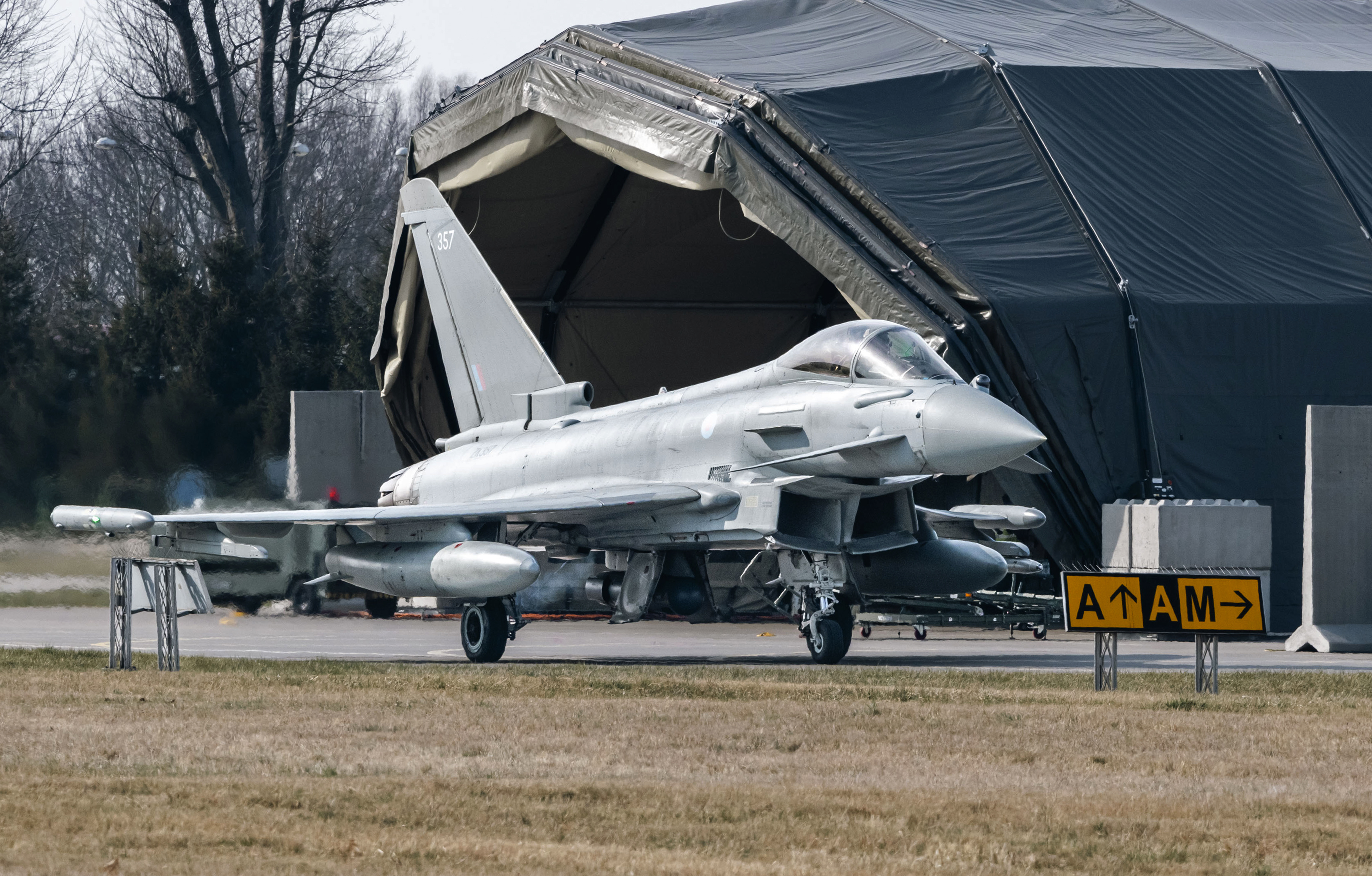 RAF Typhoons taxing on the ground with a hangar in the background.