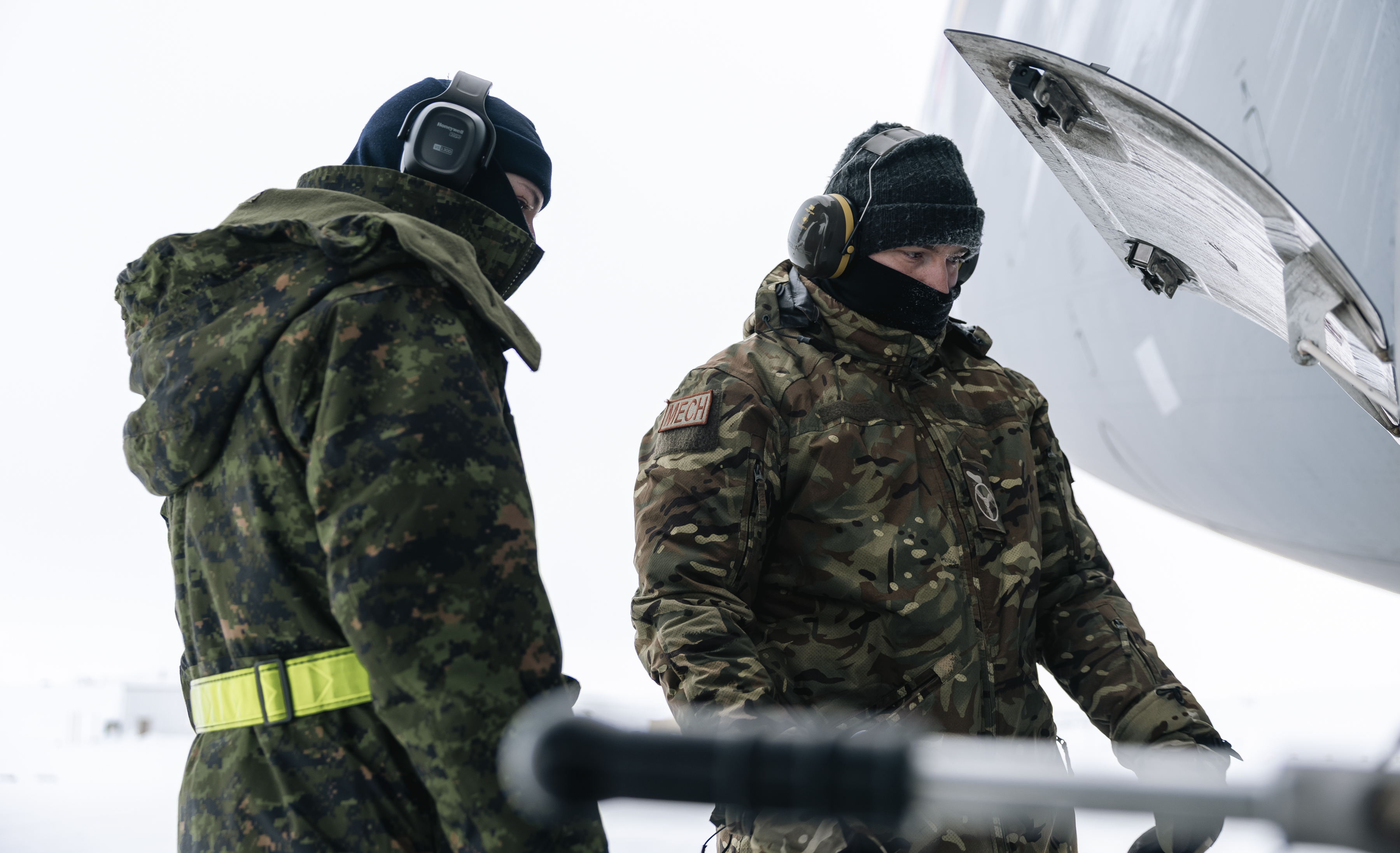 A British and Canadian serviceperson working on an aircraft in frozen conditions.