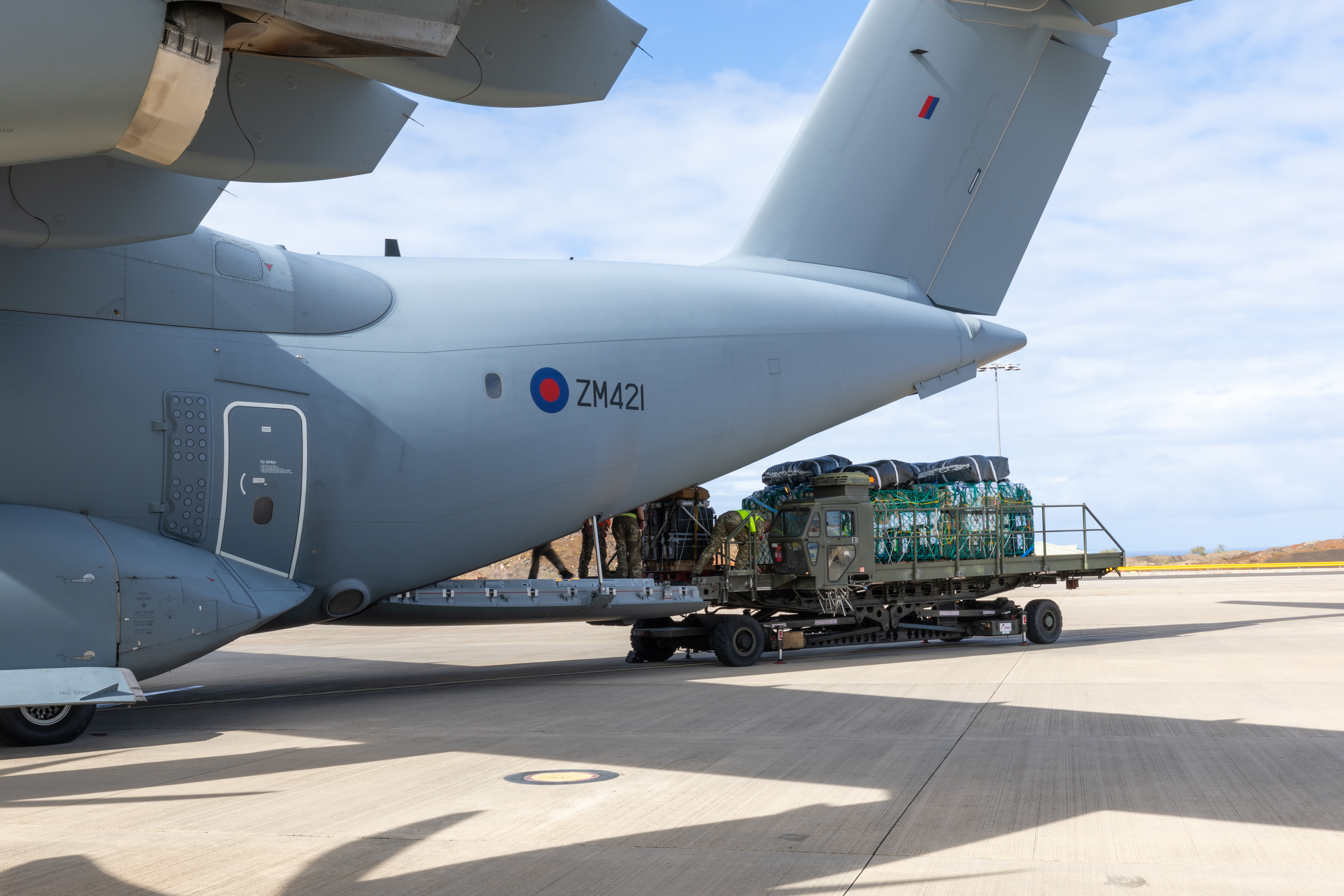 Side view of an A400M Atlas with rear ramp lowered while personnel load palletised cargo using a mechanical loader.