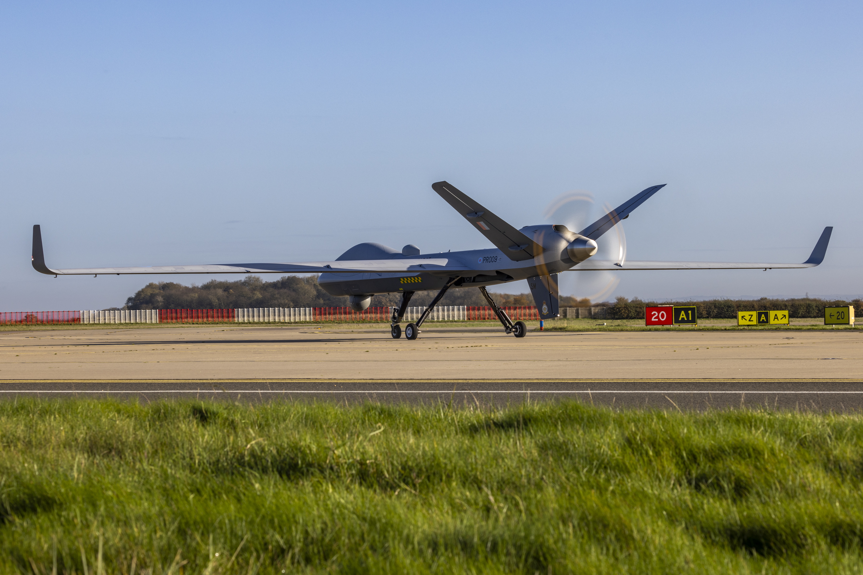 An RAF Protector parked on a runway with grass in the foreground.