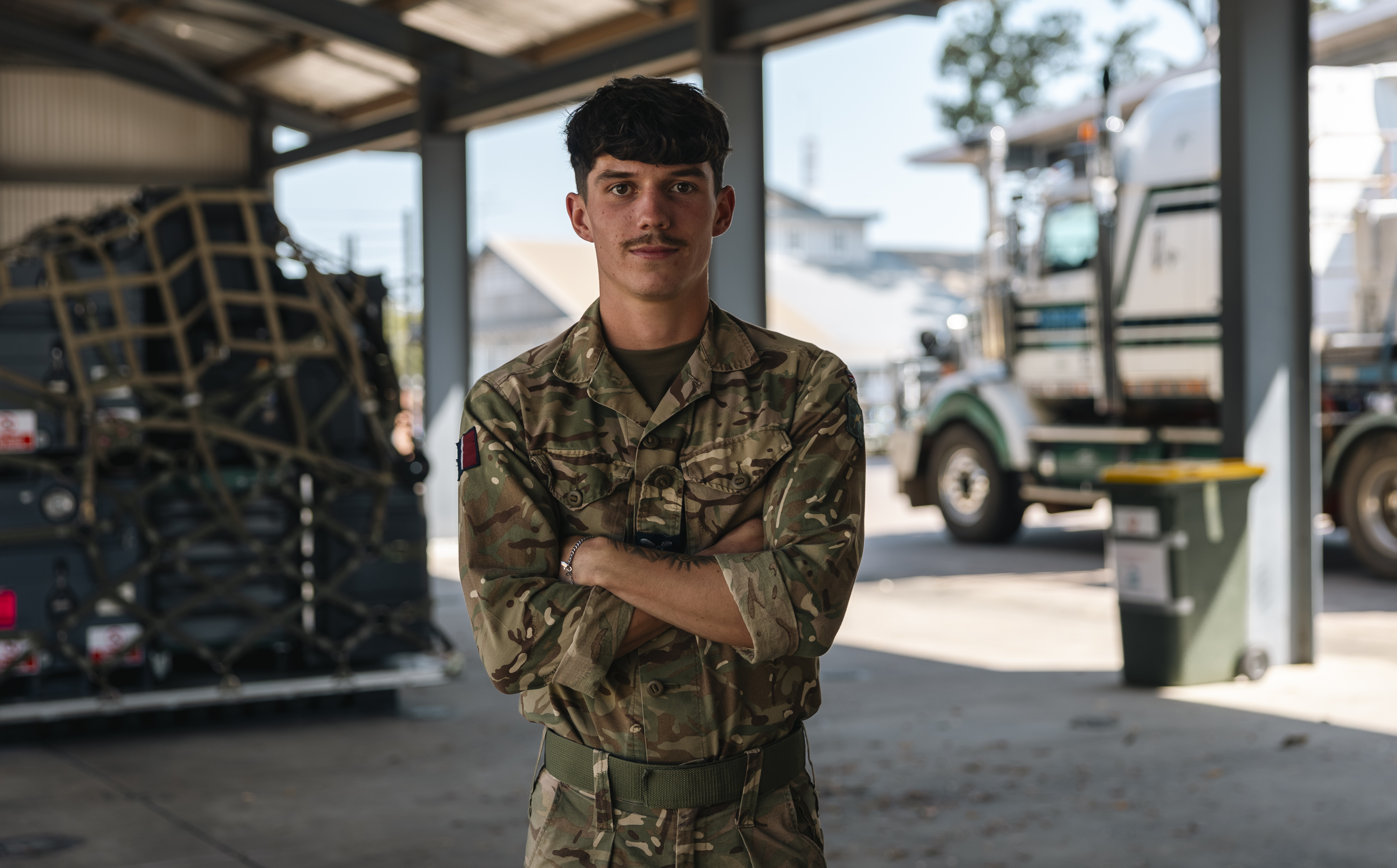 Elliot pictured with his arms crossed looking at the camera with RAF logistics equipment in the background.