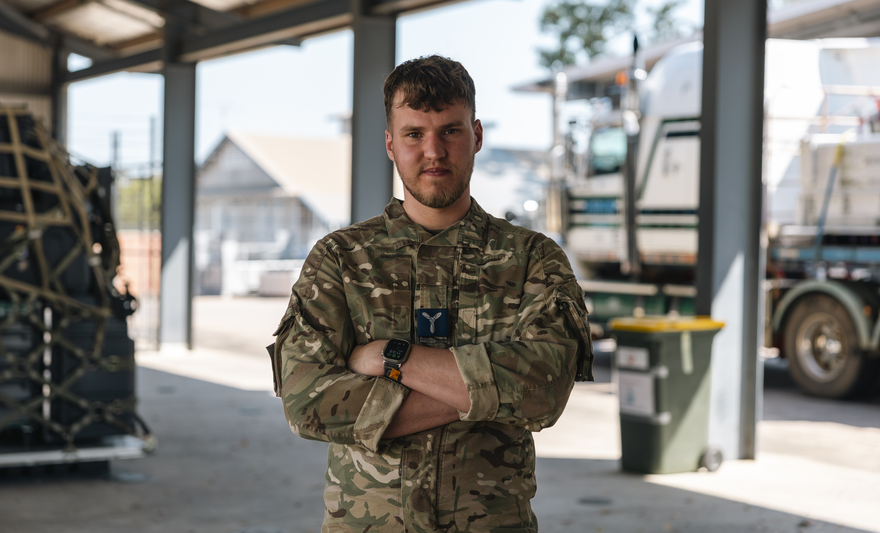 Elliot pictured with his arms crossed looking at the camera with RAF logistics equipment in the background.