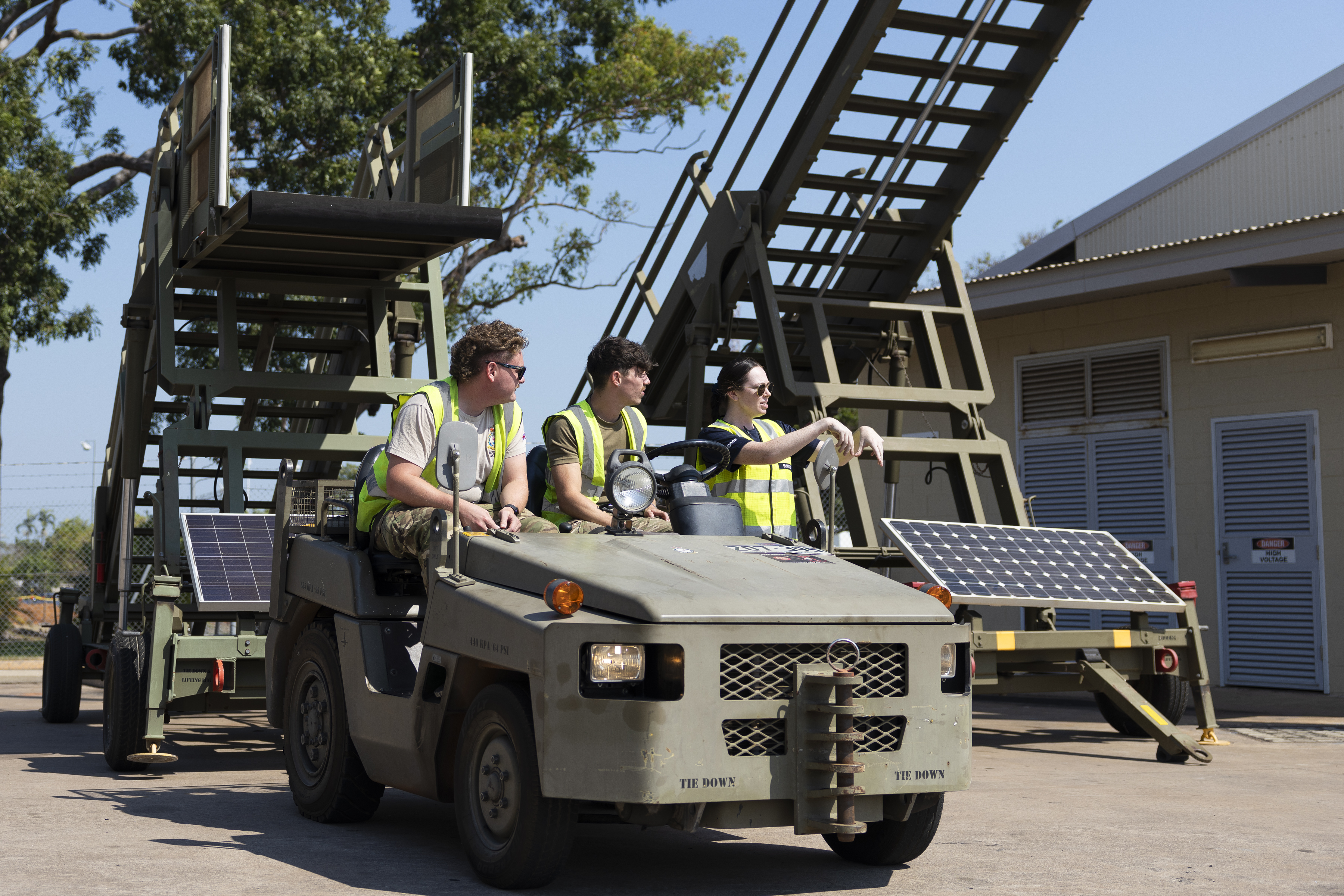 A group of three personnel sat on an airport transport vehicle with mobile passenger boarding stairs in the background.