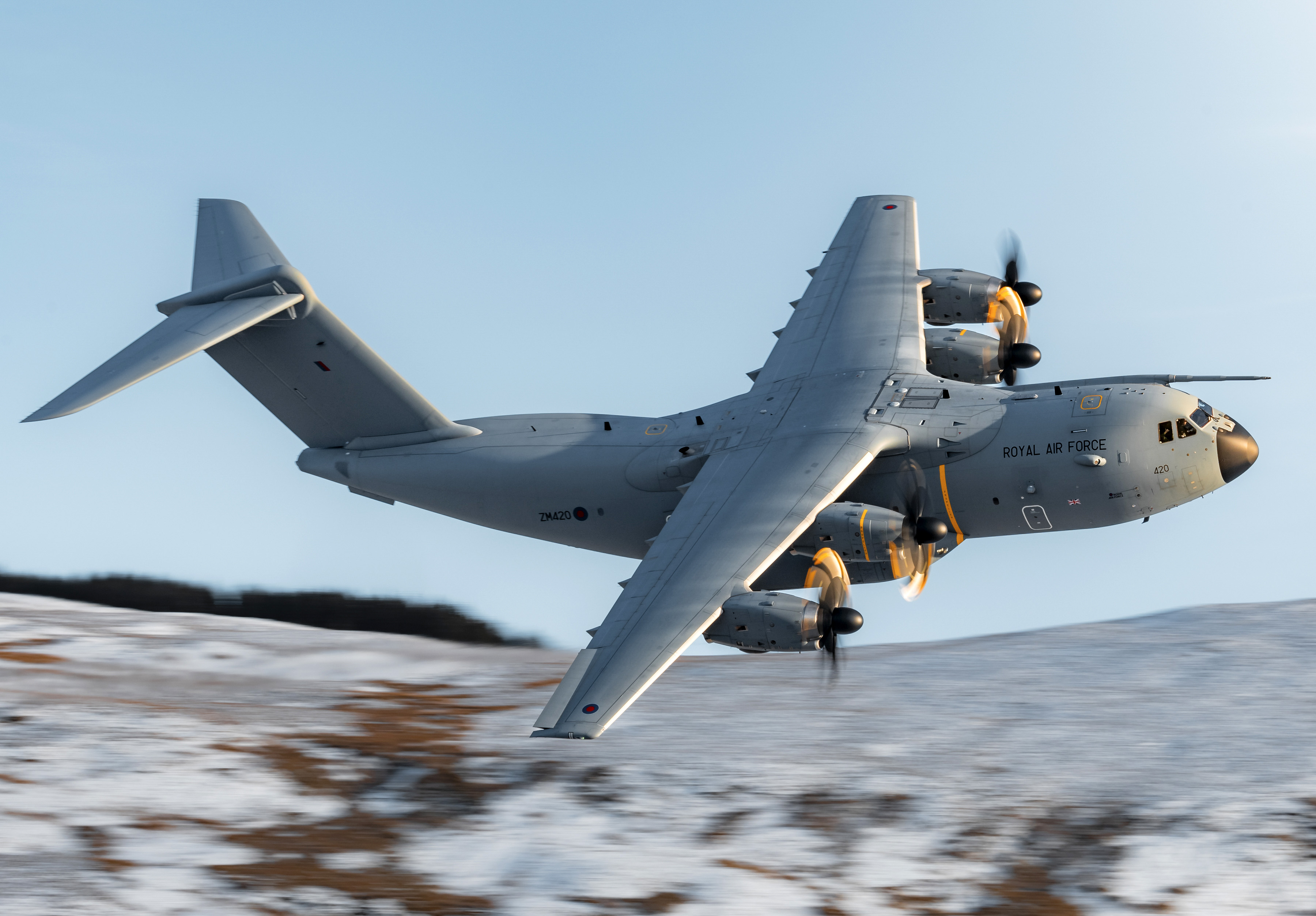An RAF A400M flies at low-level against a snowy landscape.