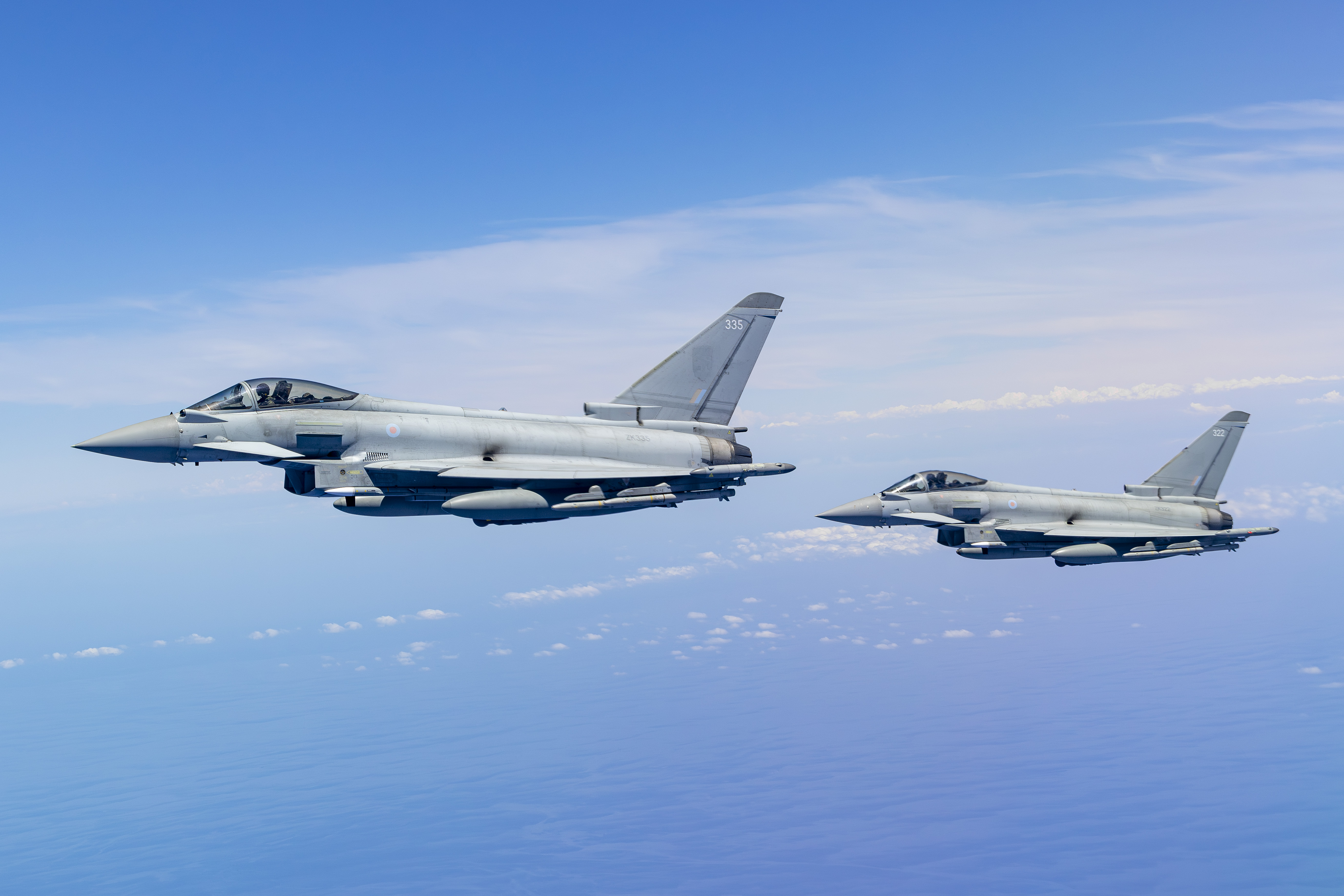 Two RAF Typhoons fitted with APKWS in flight through cloudy blue skies.