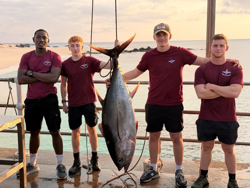 2 PARA on Georgetown pier, holding a very large, yellow fin tuna with the sea and sun setting in the background.