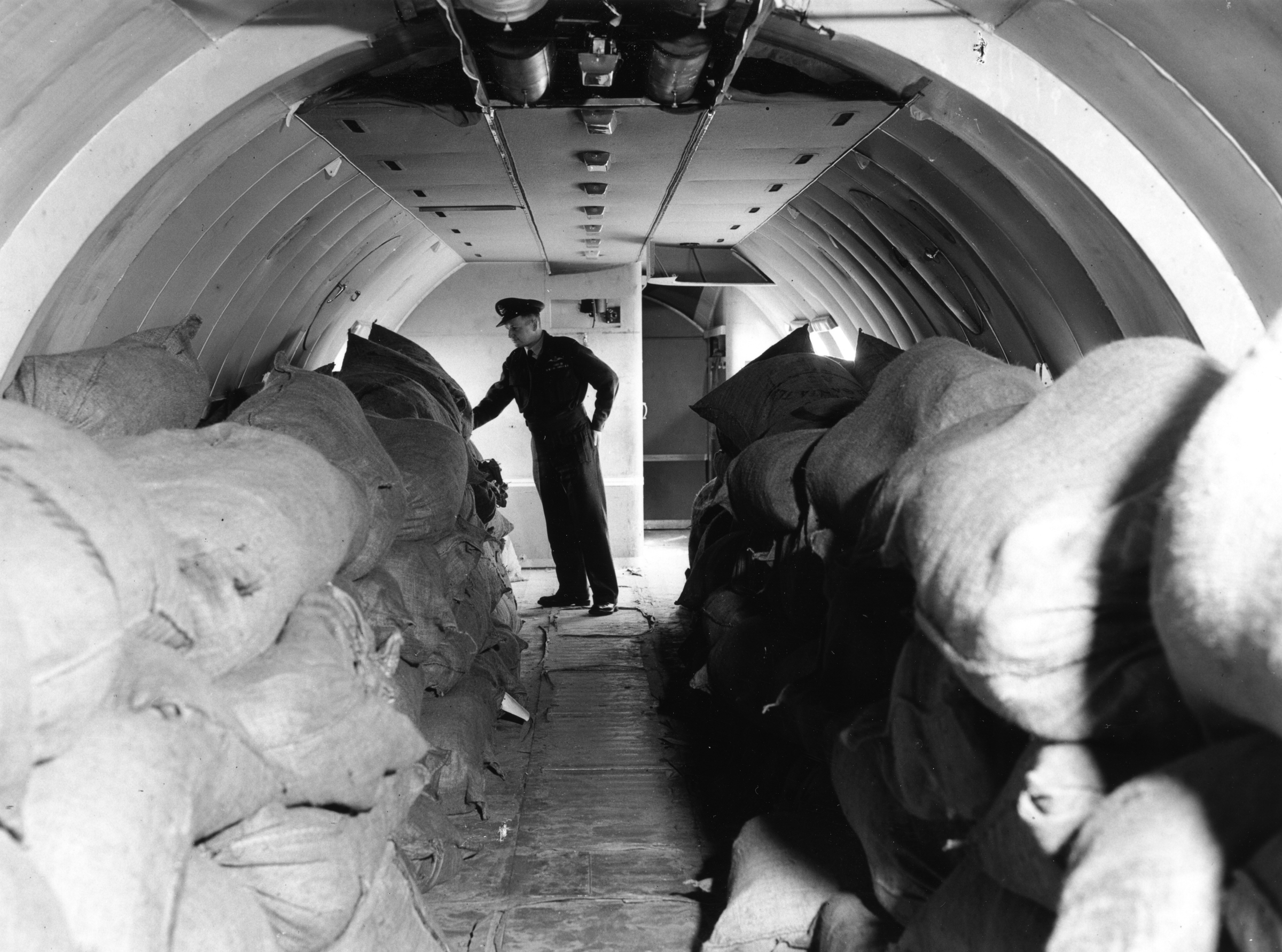 Black and white image shows sacks of aid inside an aircraft with an RAF man at the back.