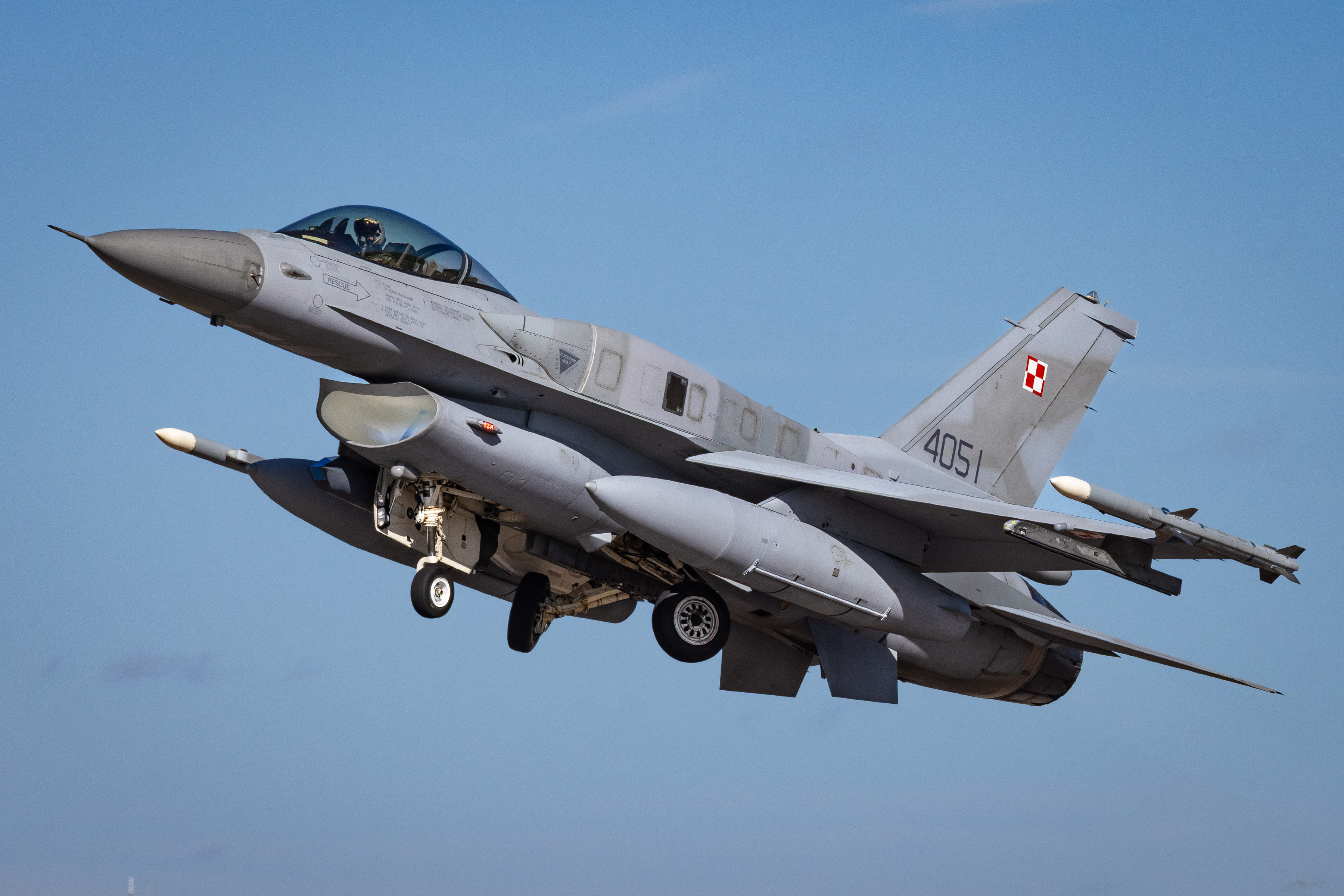 A Polish Air Force F-16 fighter jet in flight through blue skies.
