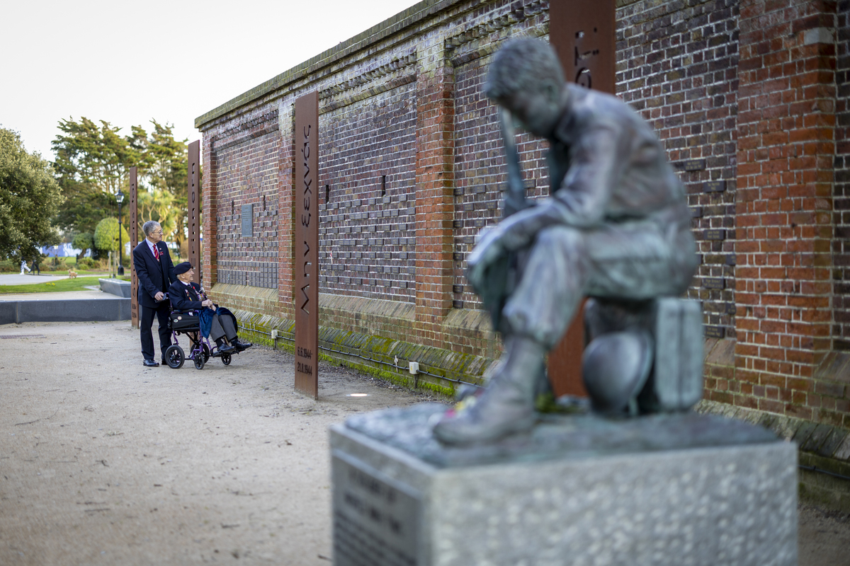 Veteran looking at the Memorial Wall, with statue in the foreground.